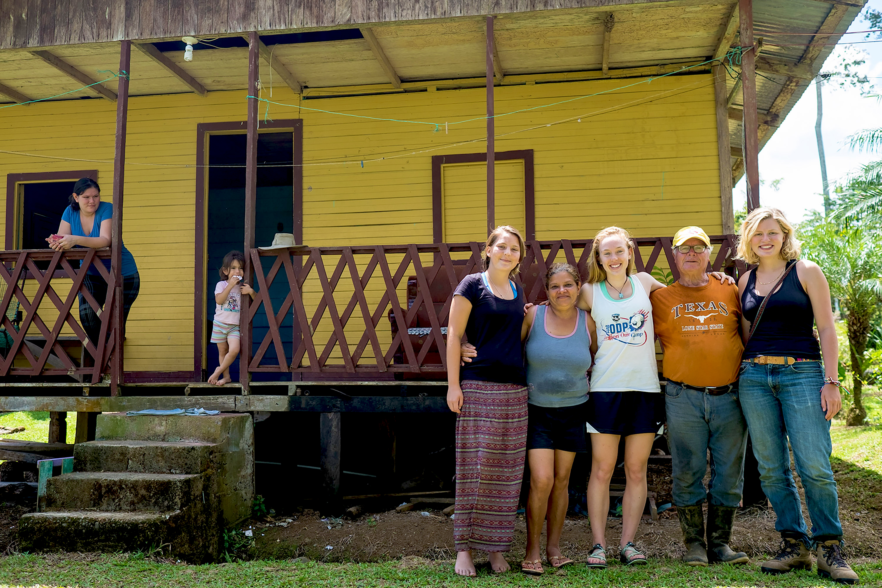 Students and their host family in front of a yellow wooden house