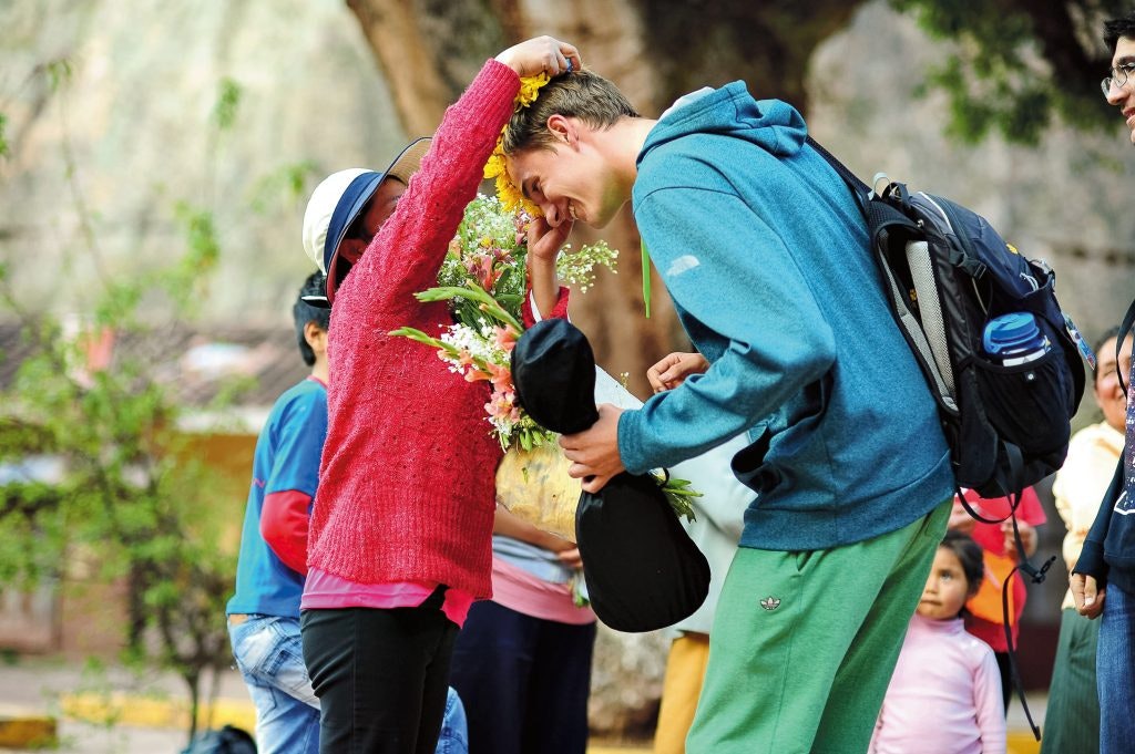 A local woman puts a flower lei over a student traveler's head during a cultural immersion experience on a gap year program.