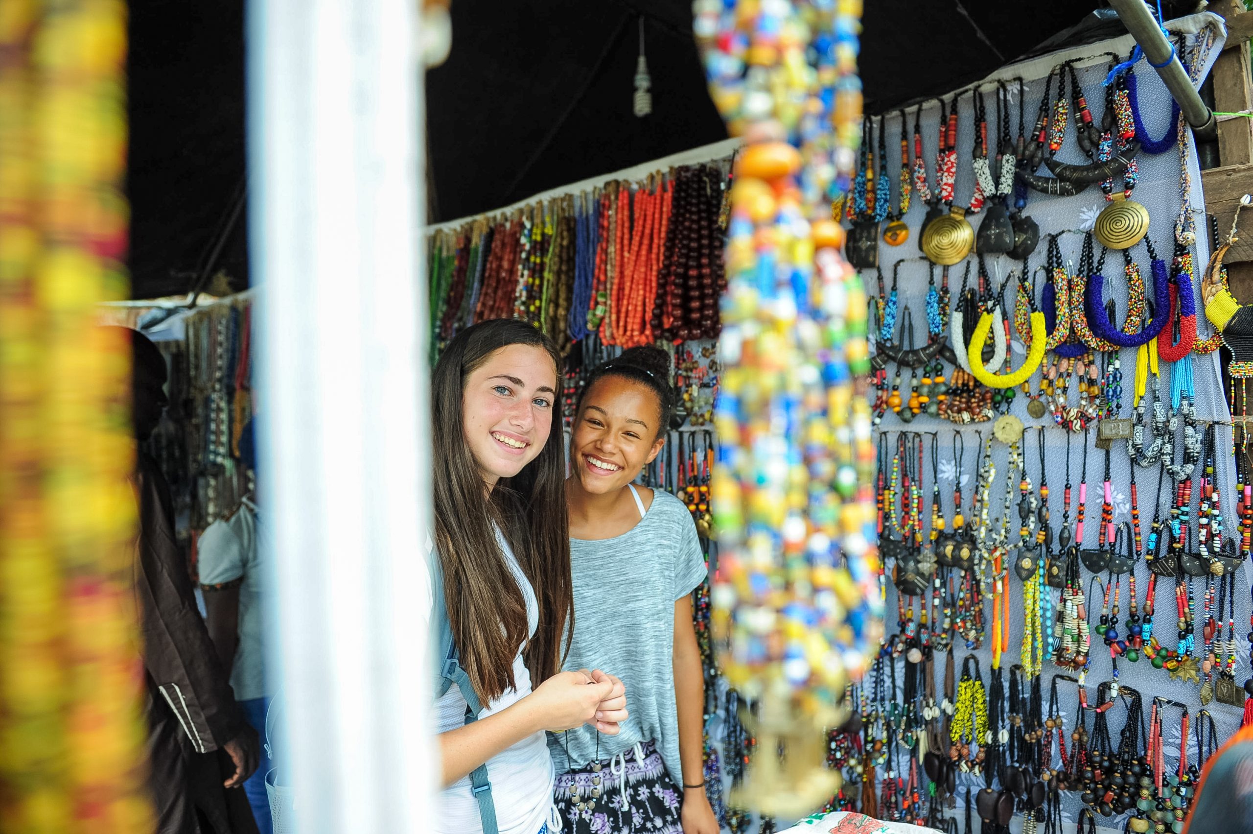 Students smile while browsing a market stall hung with colorful beaded necklaces