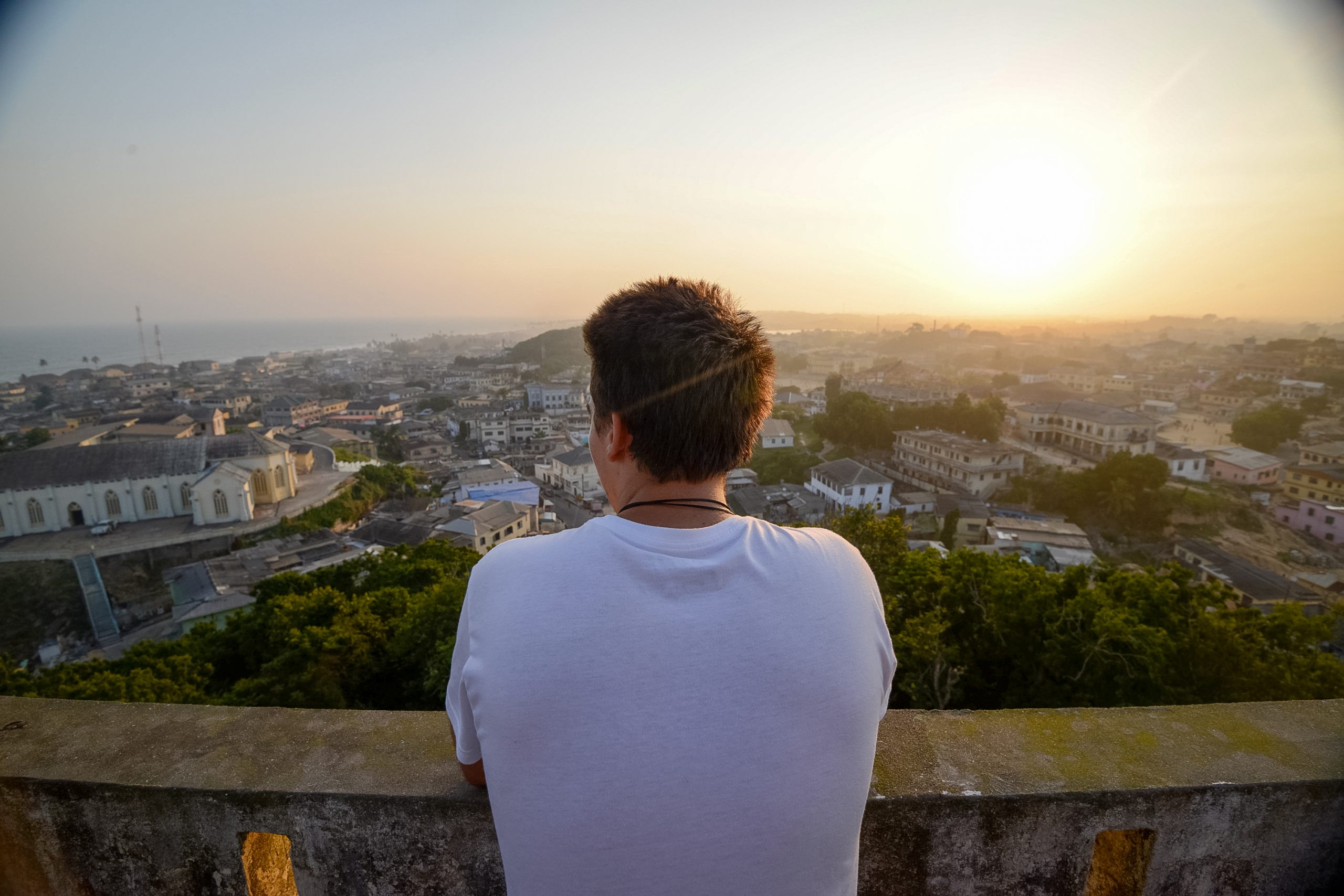 Teen travelers look out over a coastal town from a rooftop at sunset