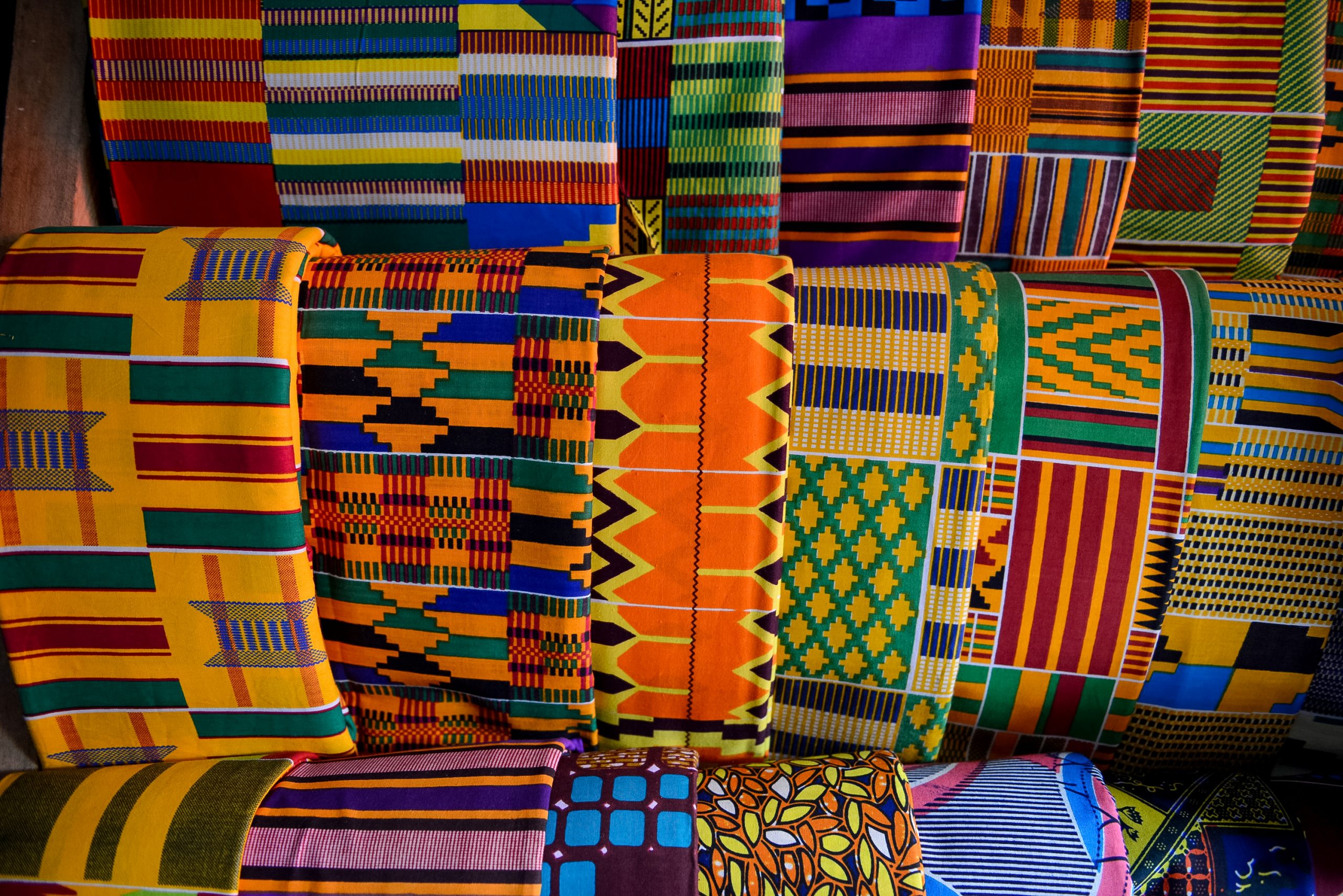 Rolled bolts of colorful kente cloth stacked on display