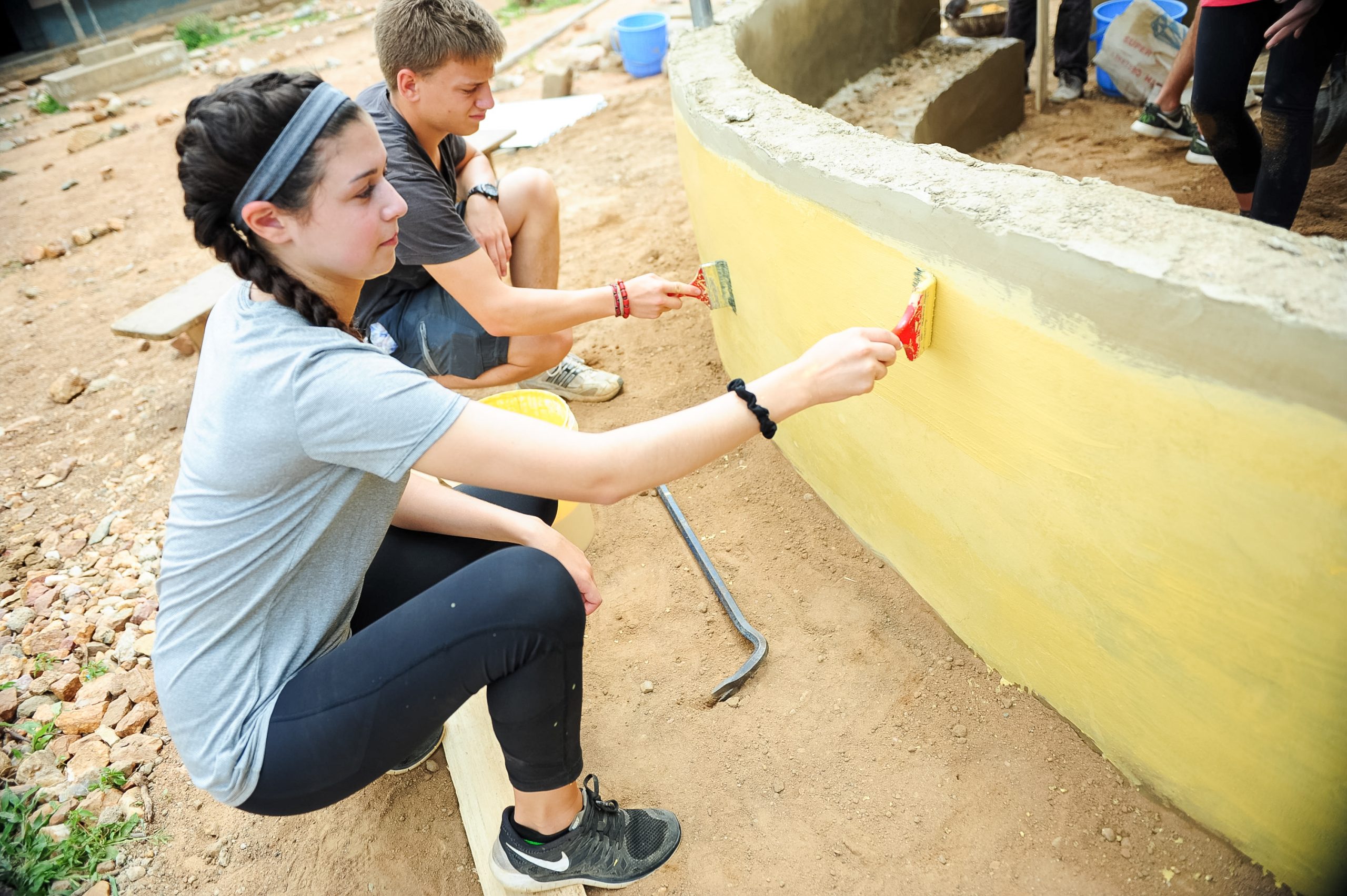 Students paint a curved concrete wall yellow at a service project site