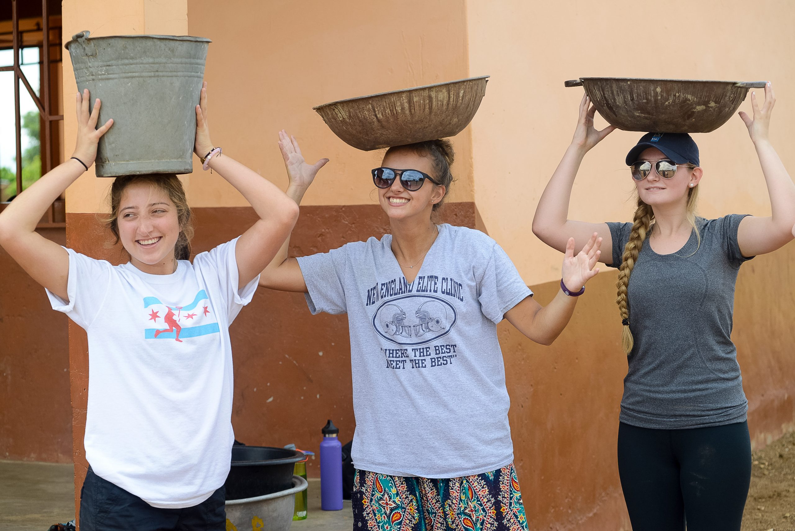Students in Ghana balance buckets and basins on their heads while smiling for the camera