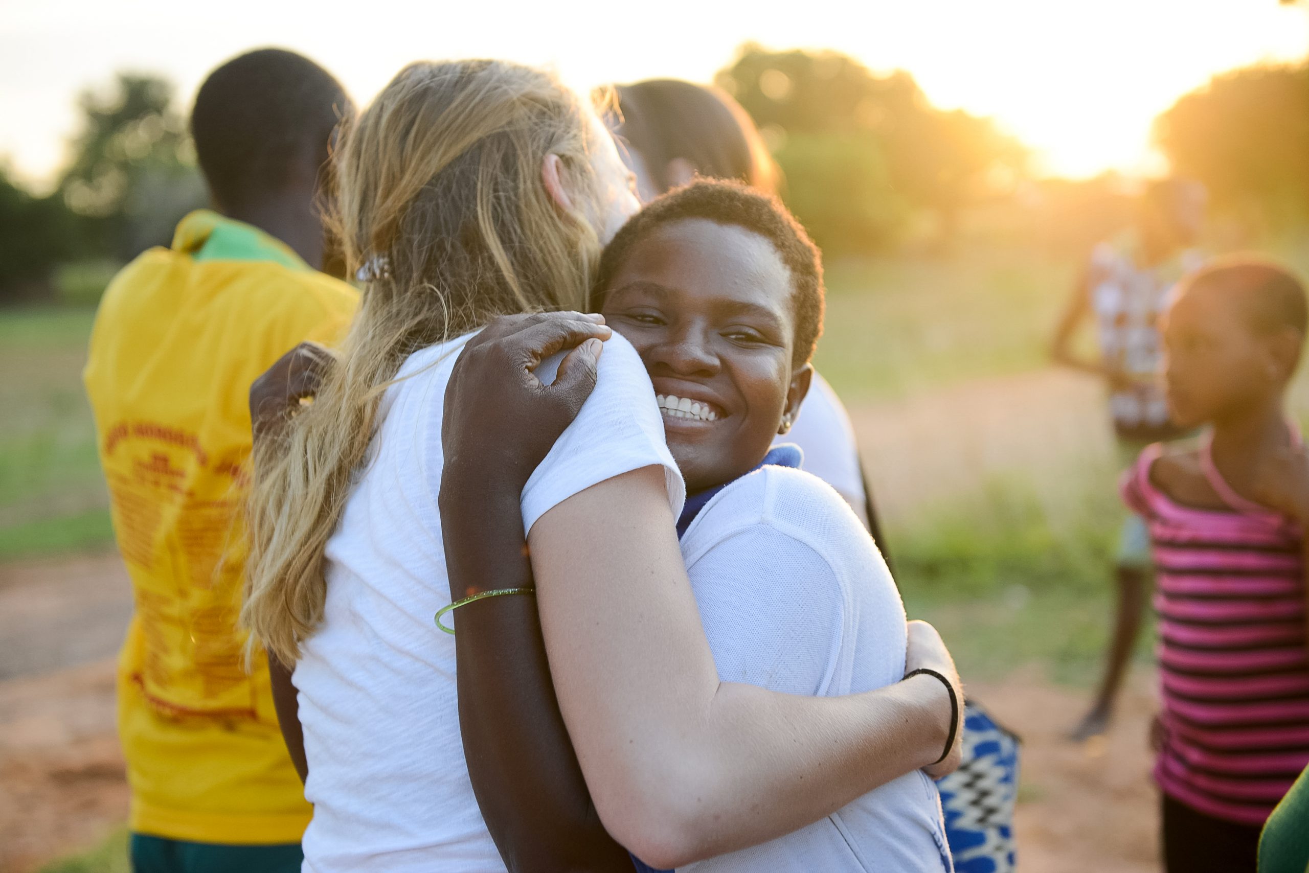 A student embraces a local girl in a warm hug at sunset