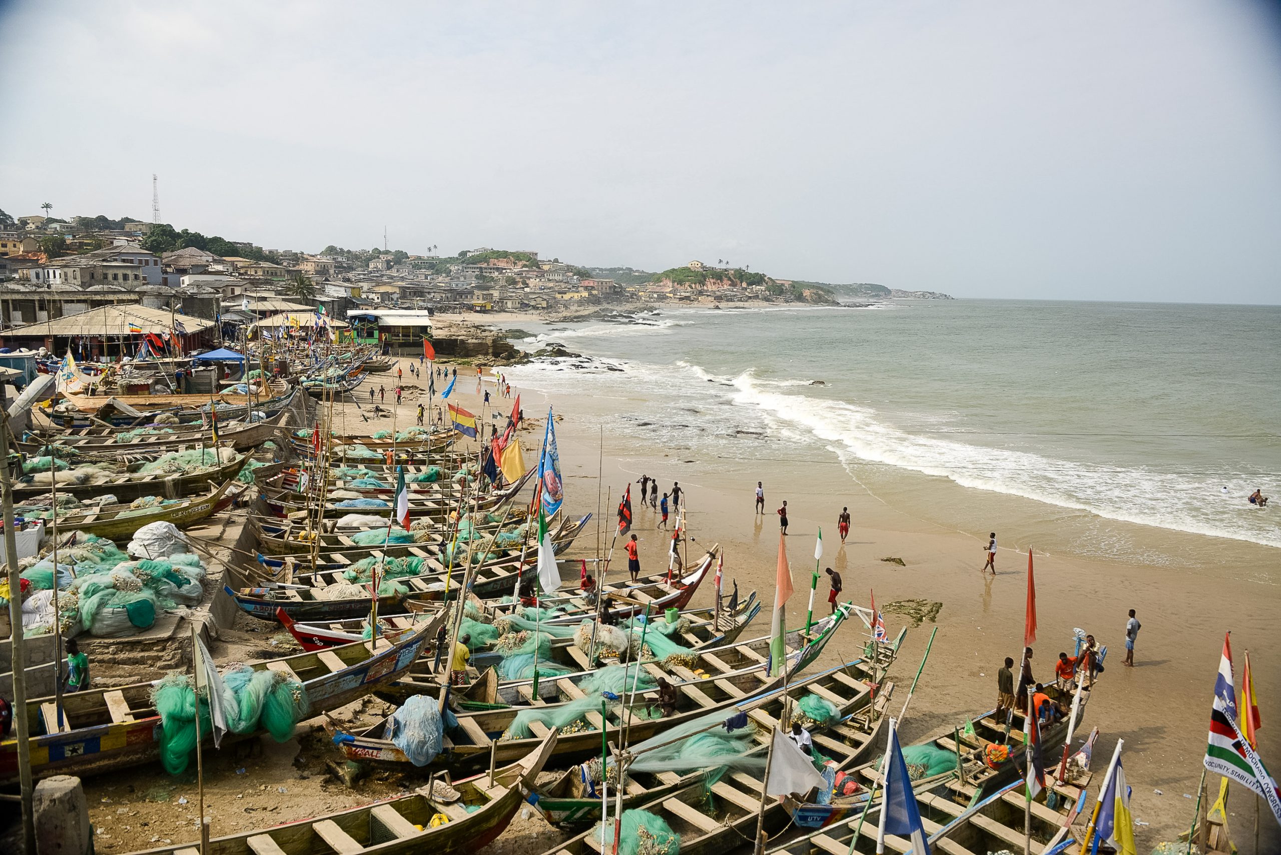 Wooden fishing boats line a sandy beach in a coastal Ghanaian fishing village