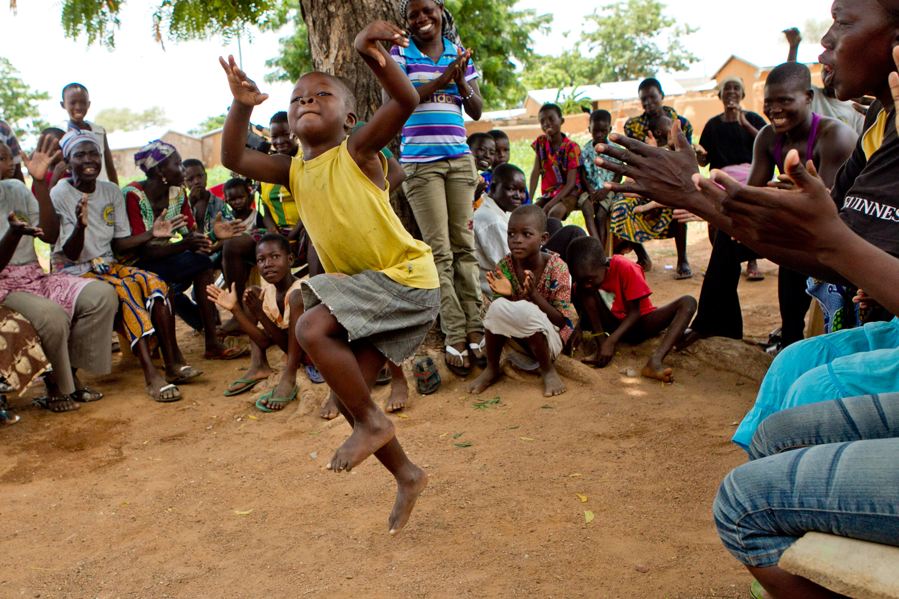 Students clap and cheer as a child dances mid-jump in the crowd