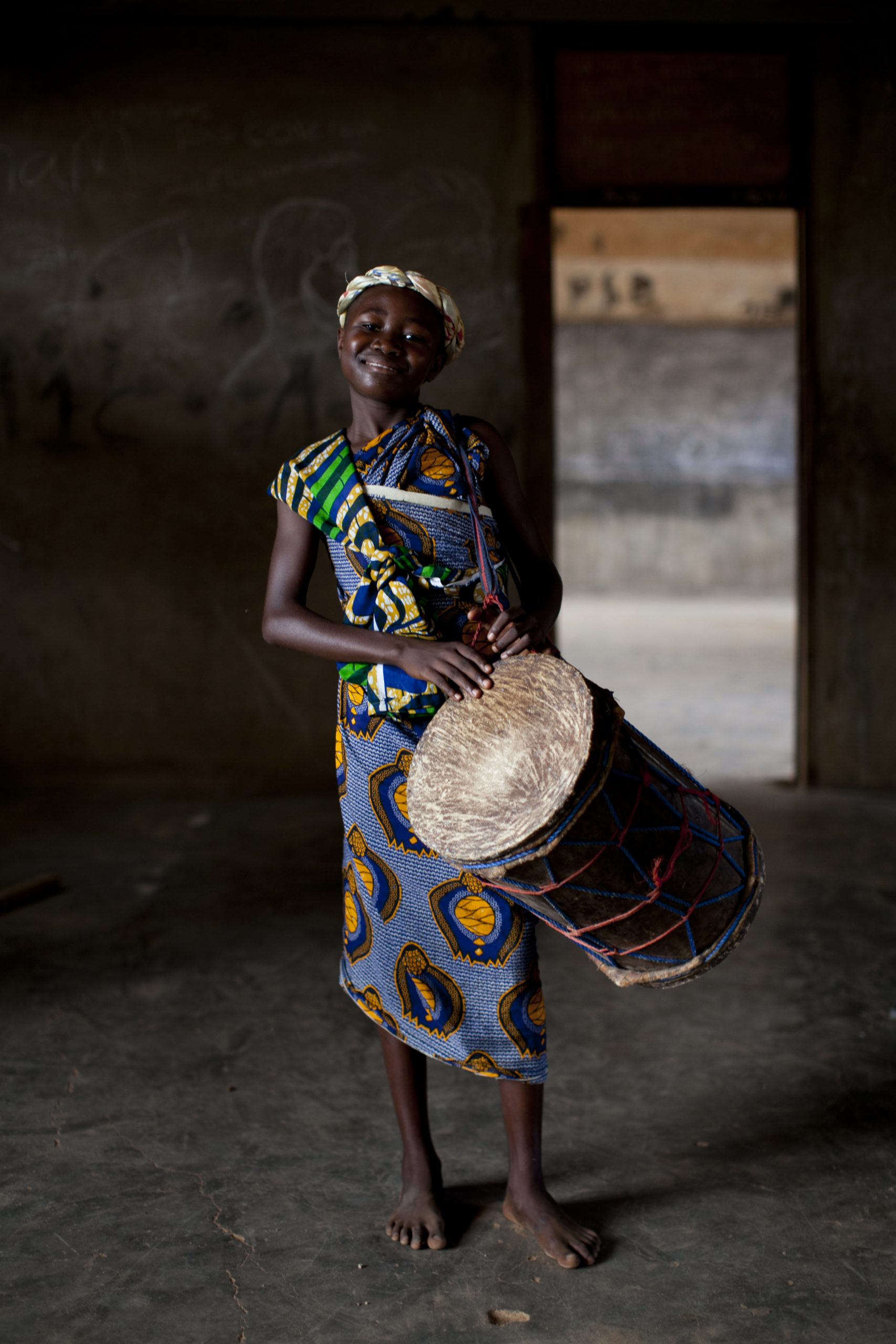 Students in traditional print dress smile while holding djembe drums