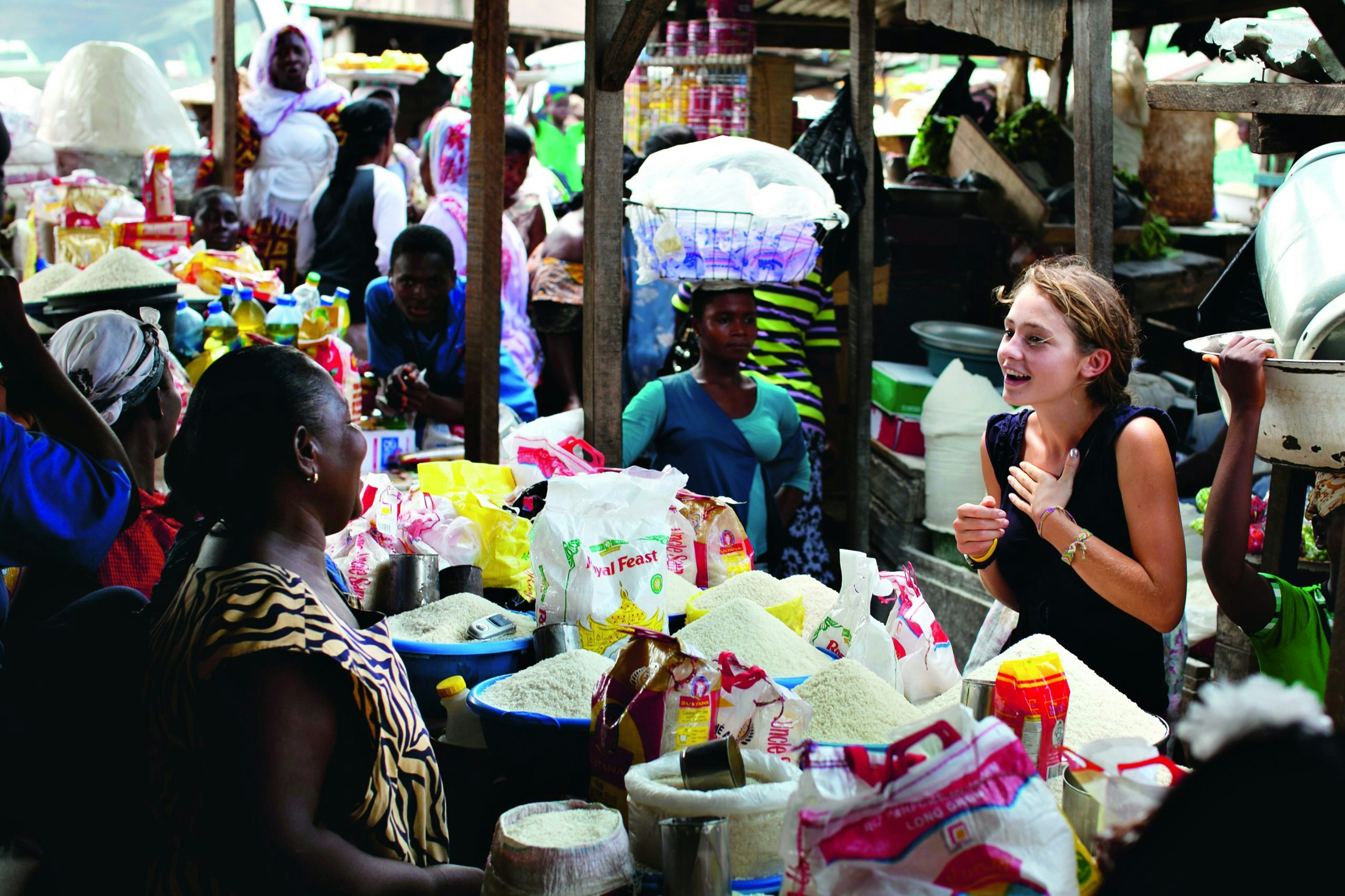 Student in a market in Ghana talking to a vendor selling grains.