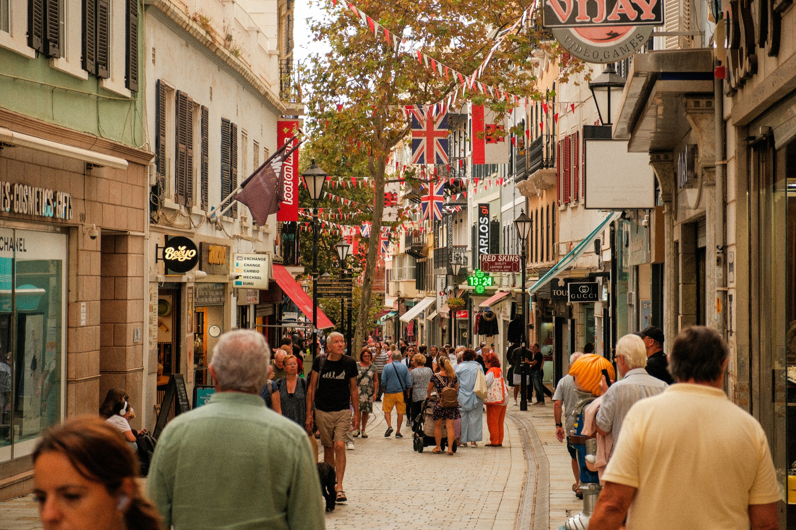 Shoppers fill a narrow pedestrian street strung with Union flags and bunting between shopfronts and balconies.