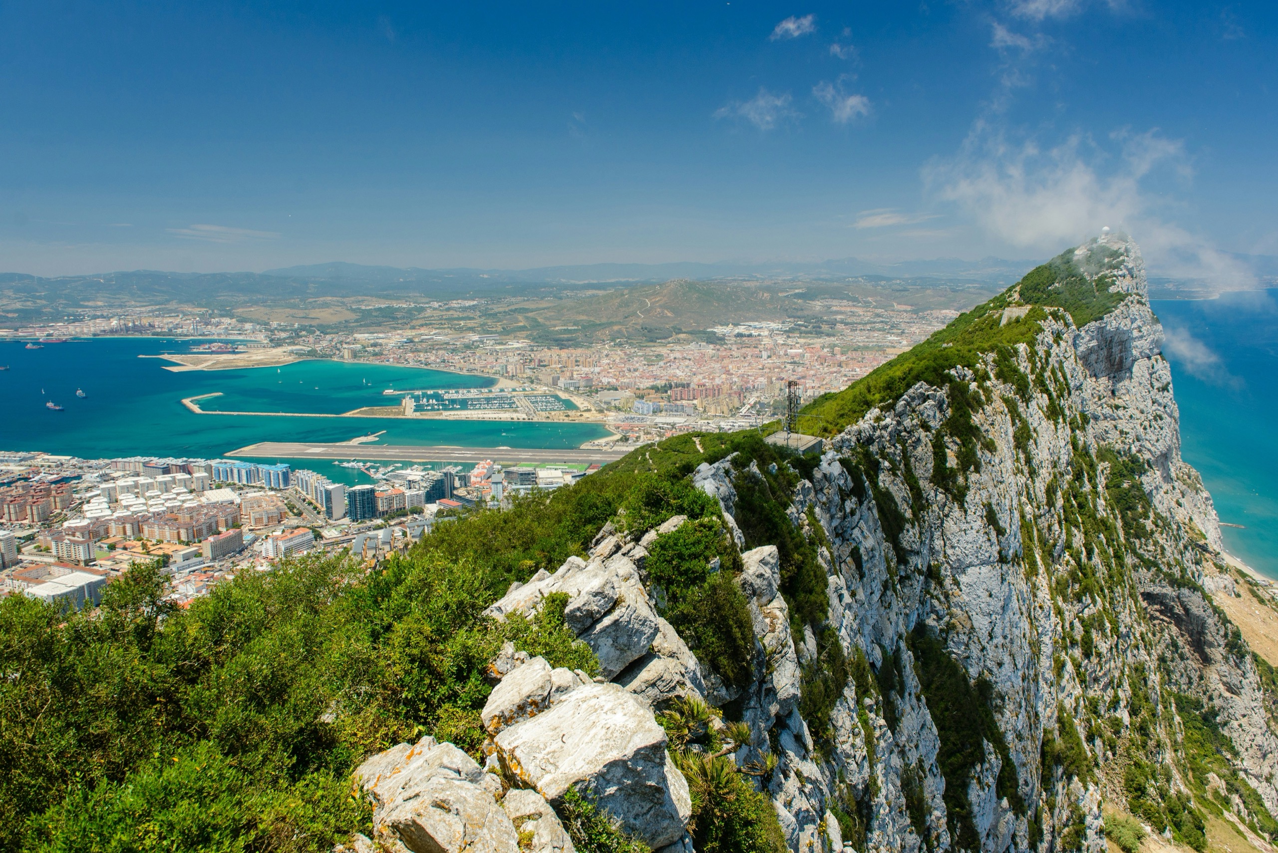 The limestone ridge of the Rock of Gibraltar drops toward the town, the airport runway and the bay, with the Spanish coast beyond.