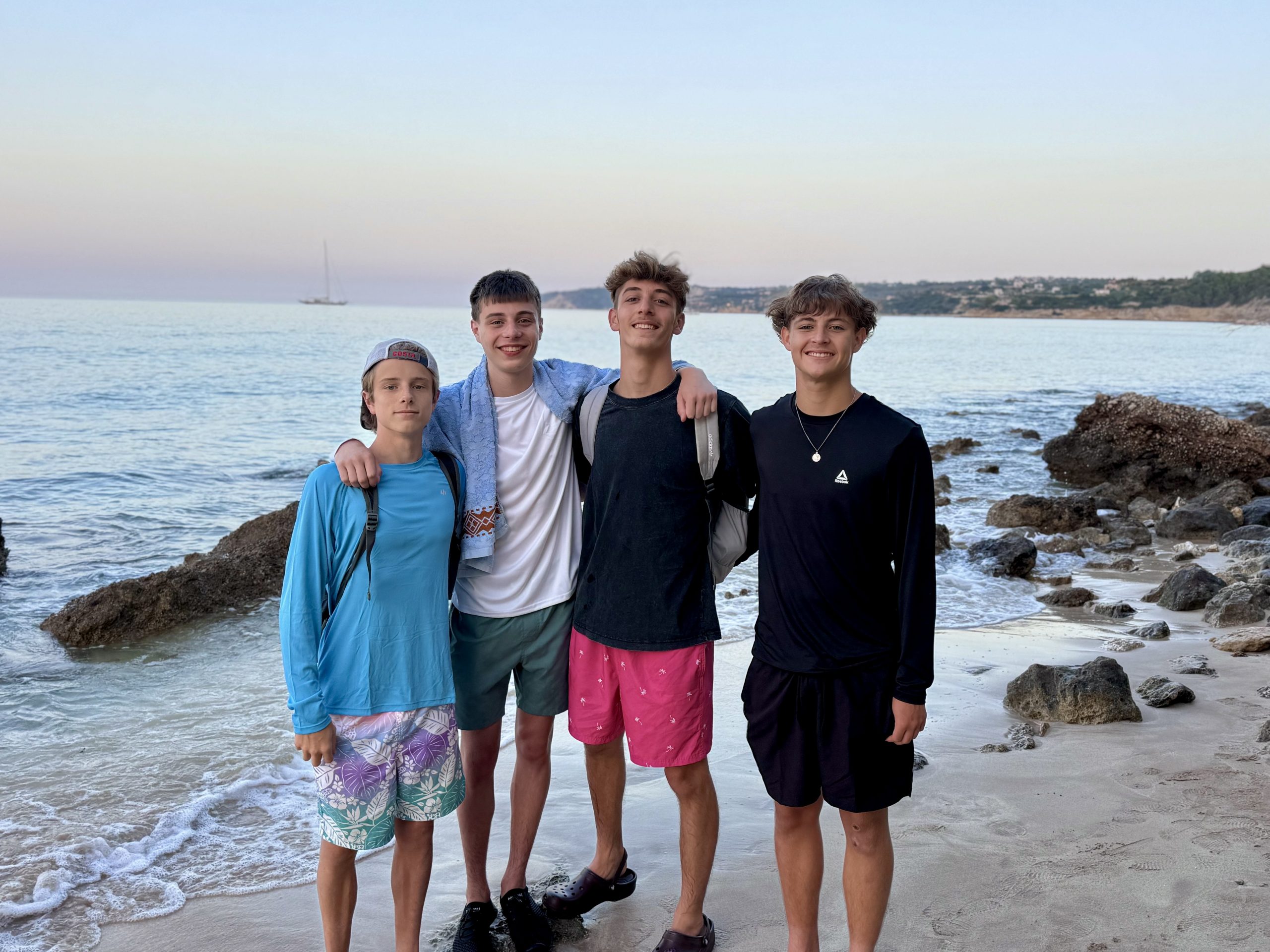 Students pose together on a rocky beach along the Greek coastline at dusk