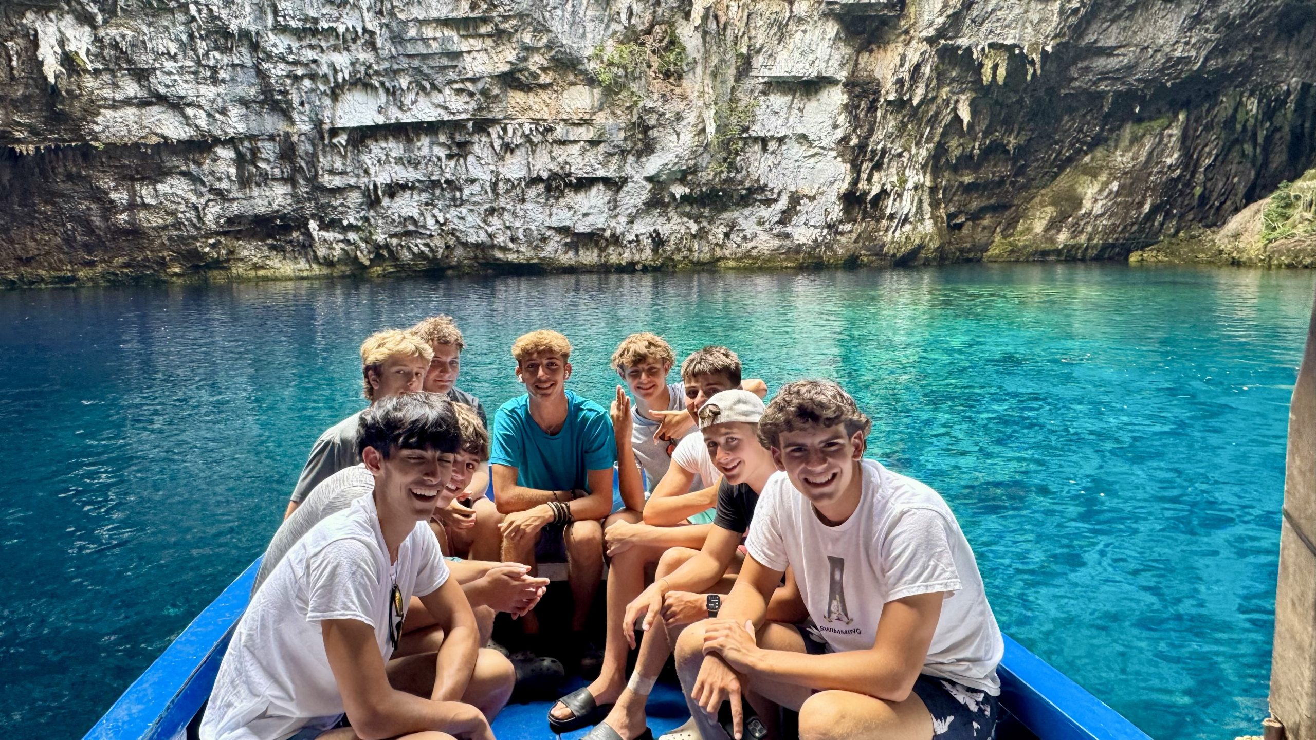 Student travelers smile aboard a boat in a rocky cove with turquoise water