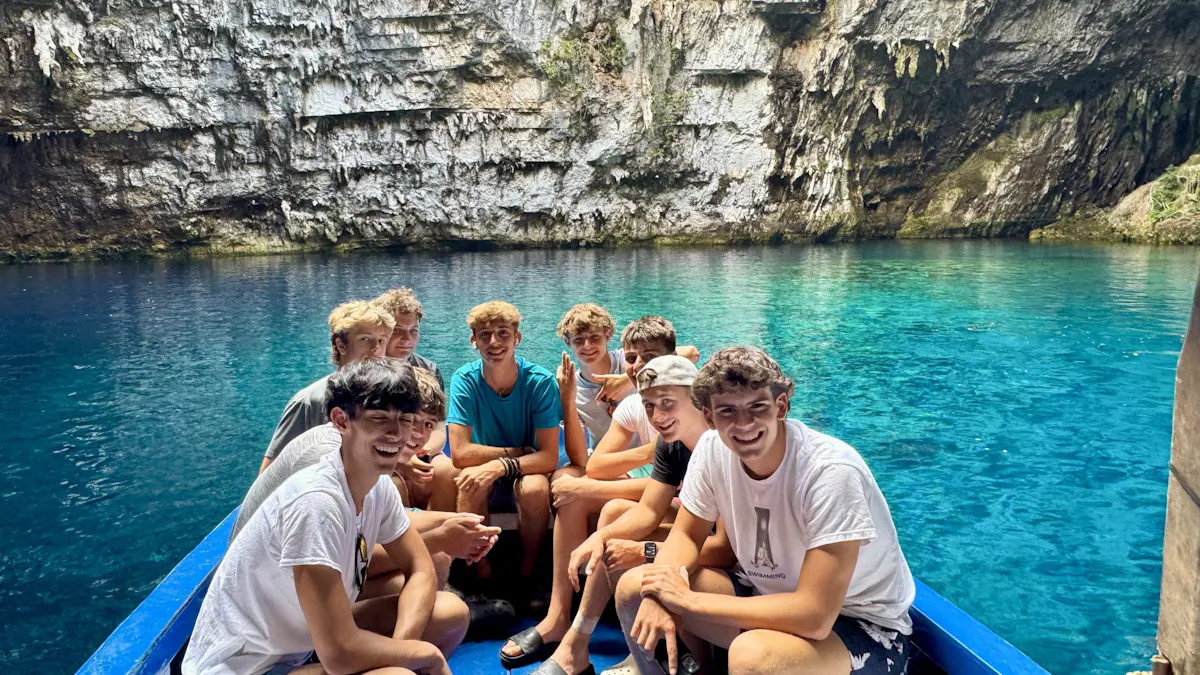 Students sitting together in a wooden boat on the clear turquoise water of a cave lake, rock walls rising behind them