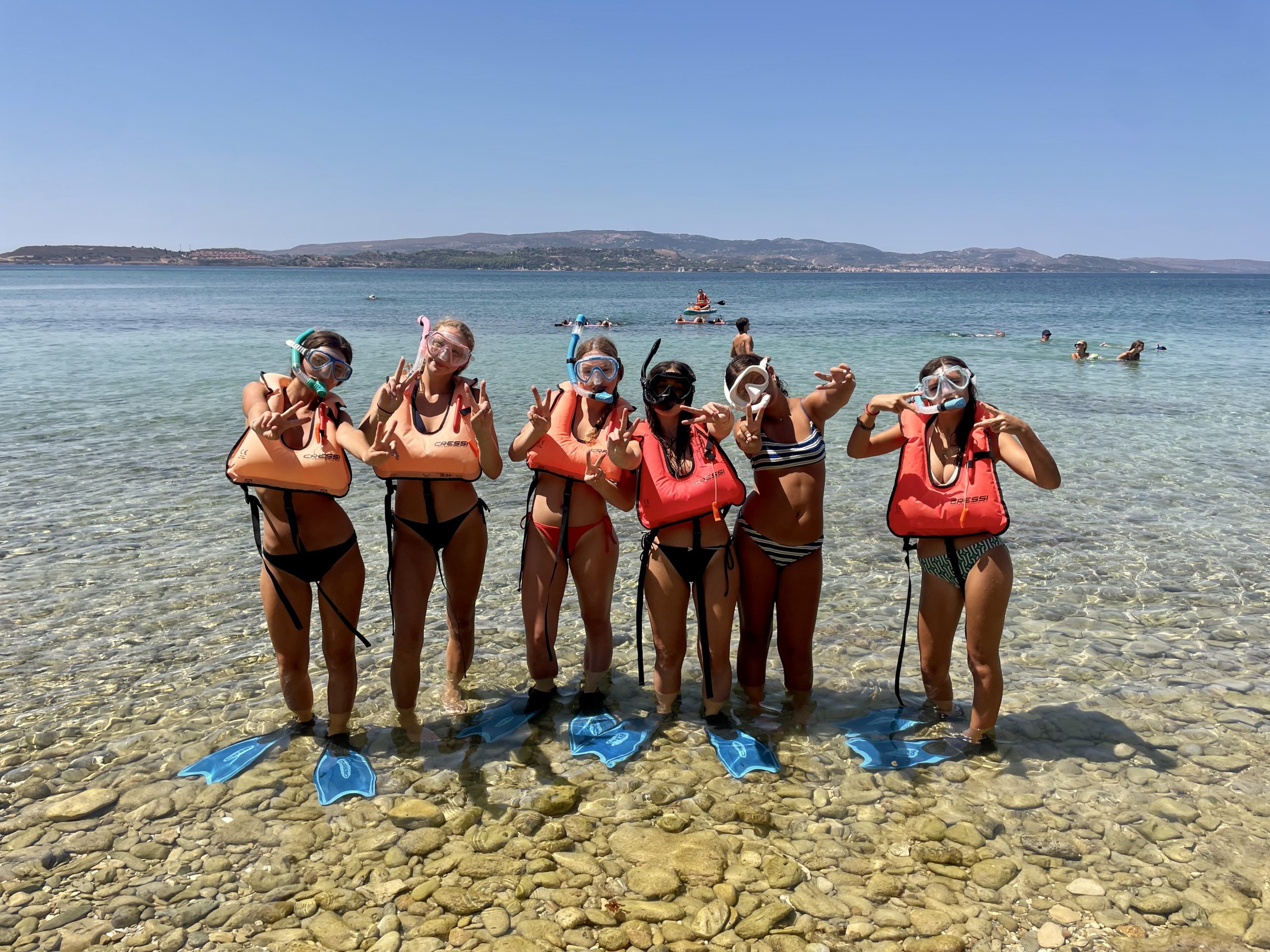 Students in snorkel masks and life vests pose on a rocky beach before swimming