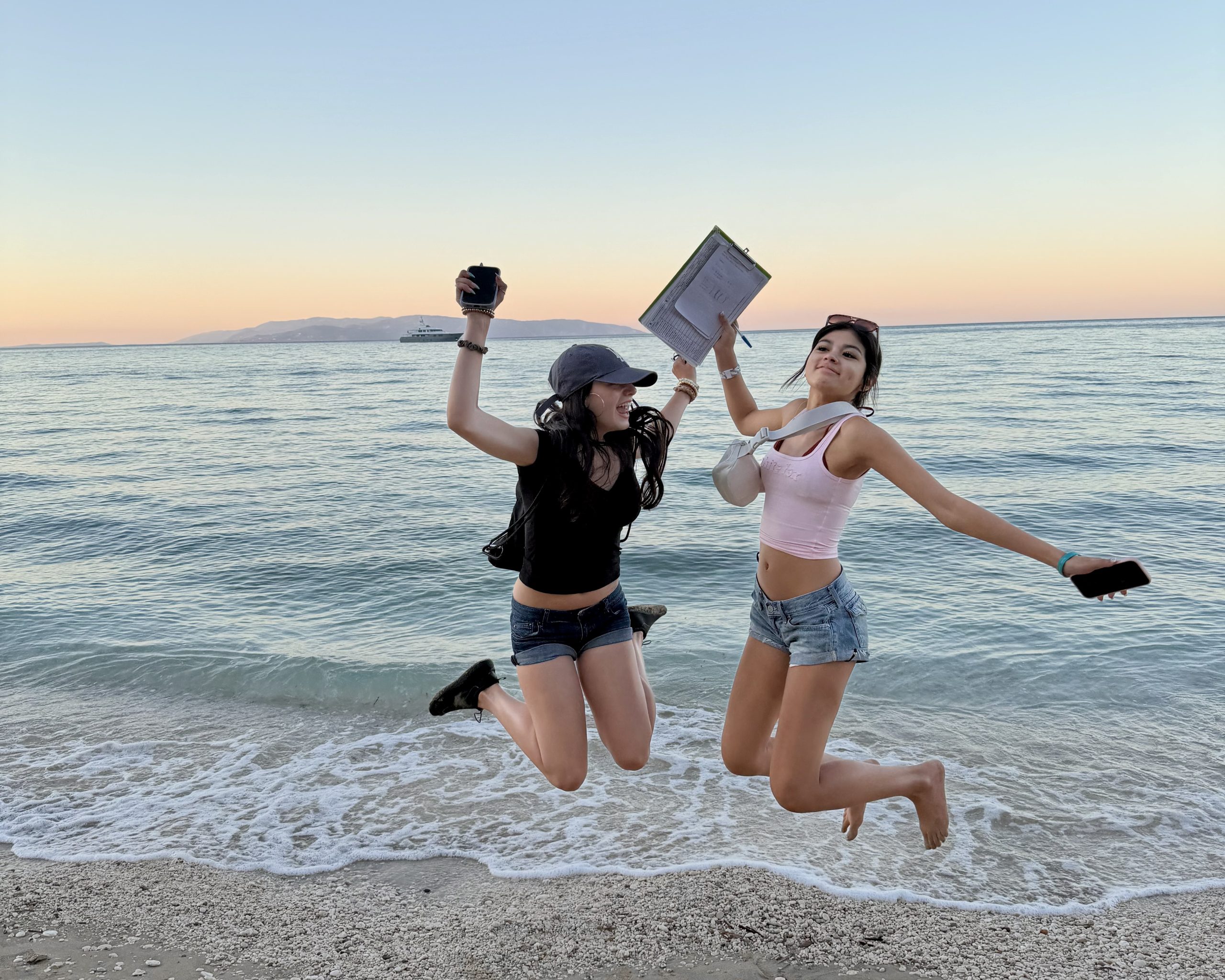 Students sitting around a taped-off sea turtle nesting site on a beach at sunrise, two staff members standing beside them and the sea behind
