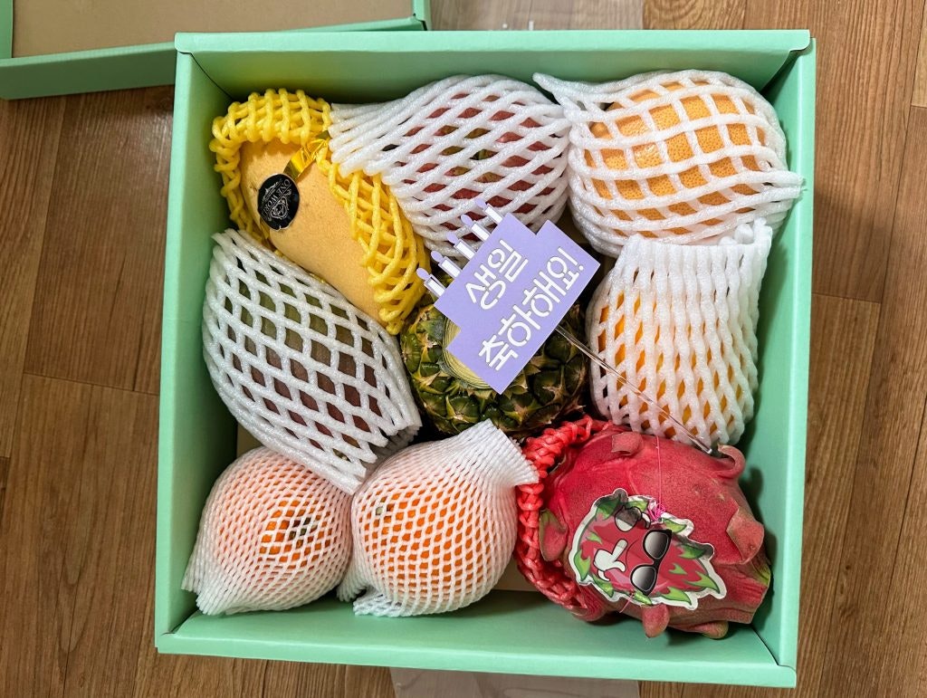A box filled with fruits covered in Styrofoam protective sleeves. Fruits include: dragon fruit, oranges, mangoes, and apples.