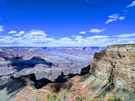A wide-angle view of the Grand Canyon under a bright blue sky with scattered clouds.