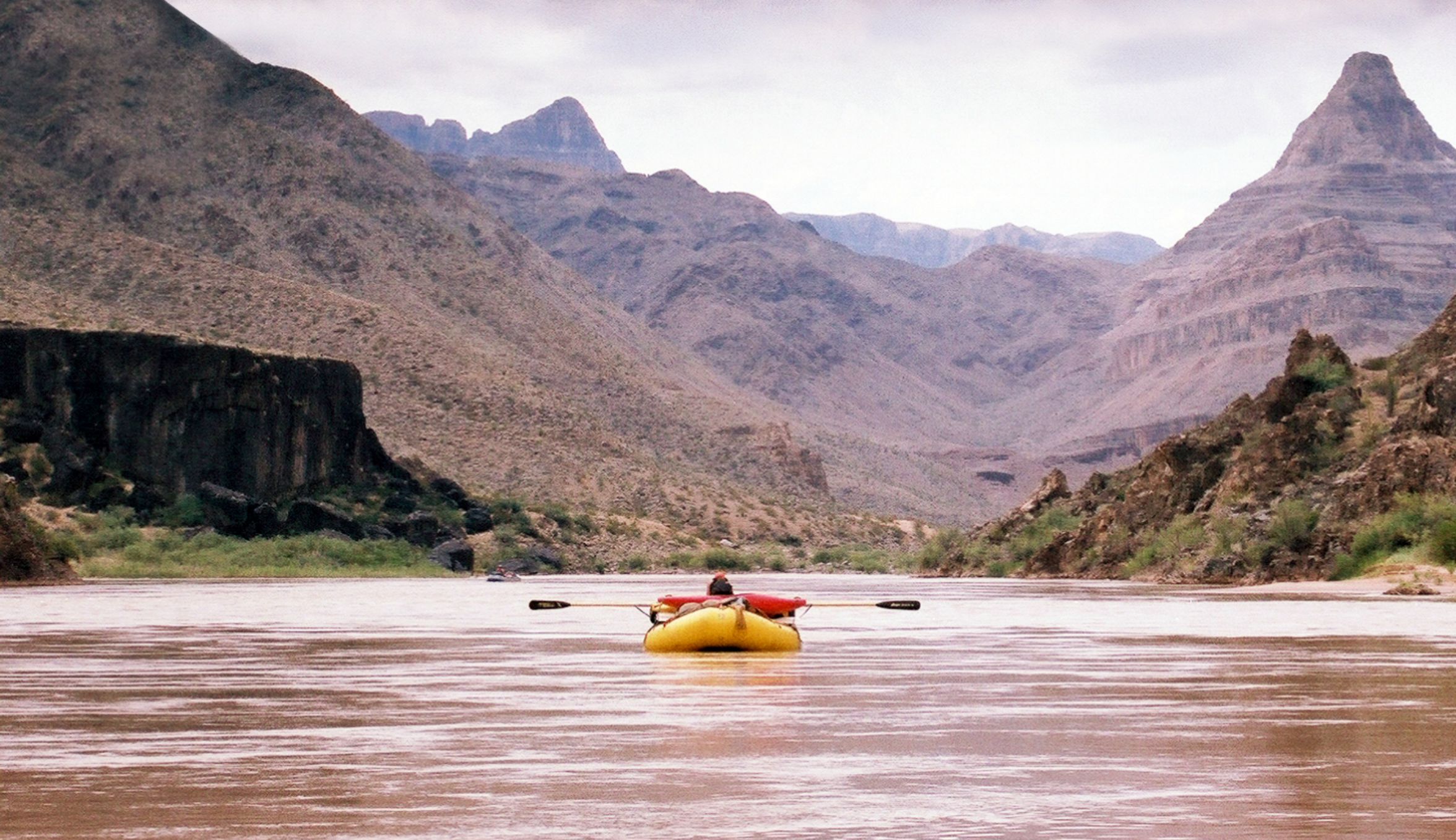 A student rafts a muddy river through a steep desert canyon