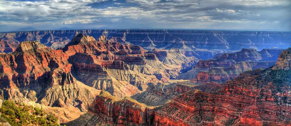 Layered red rock formations stretch across the Grand Canyon under a cloudy sky