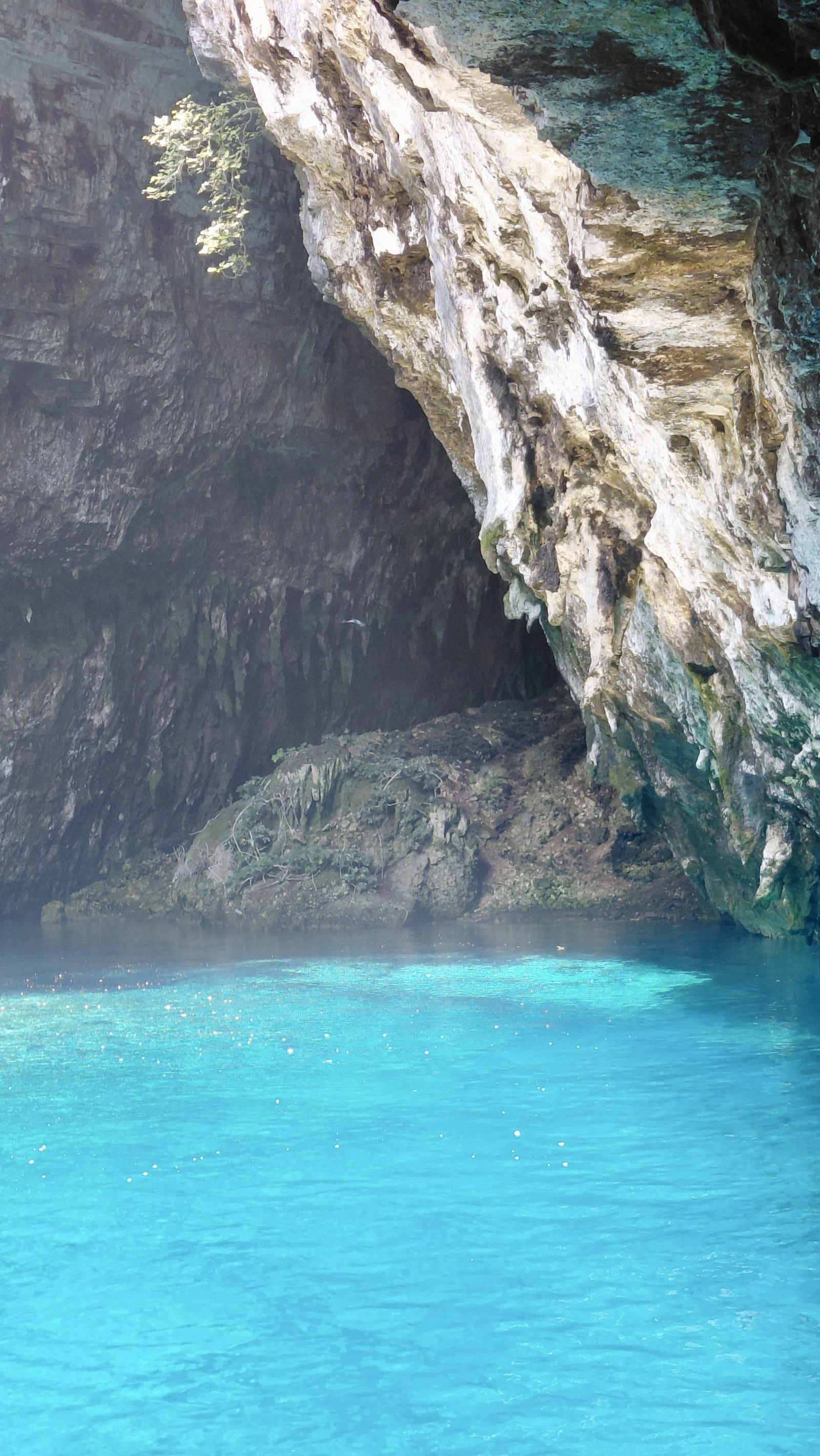 Bright turquoise water fills the mouth of a sea cave below pale limestone cliffs in Greece