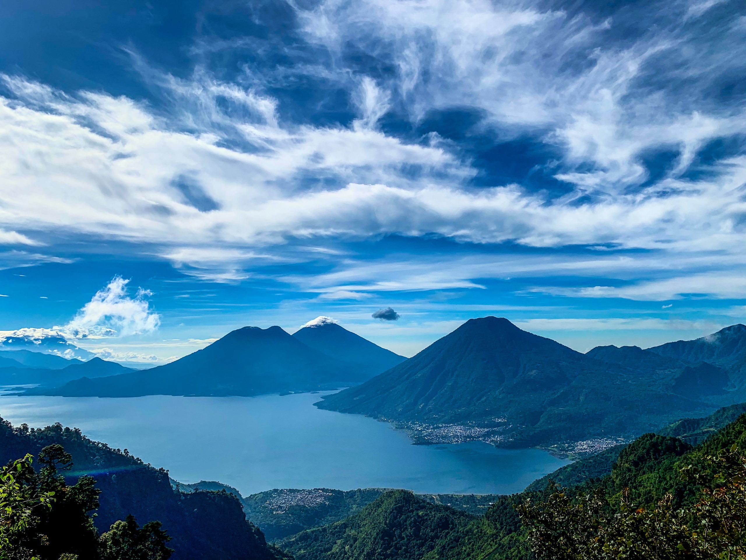 Volcanoes rise above Lake Atitlán under a wide blue sky