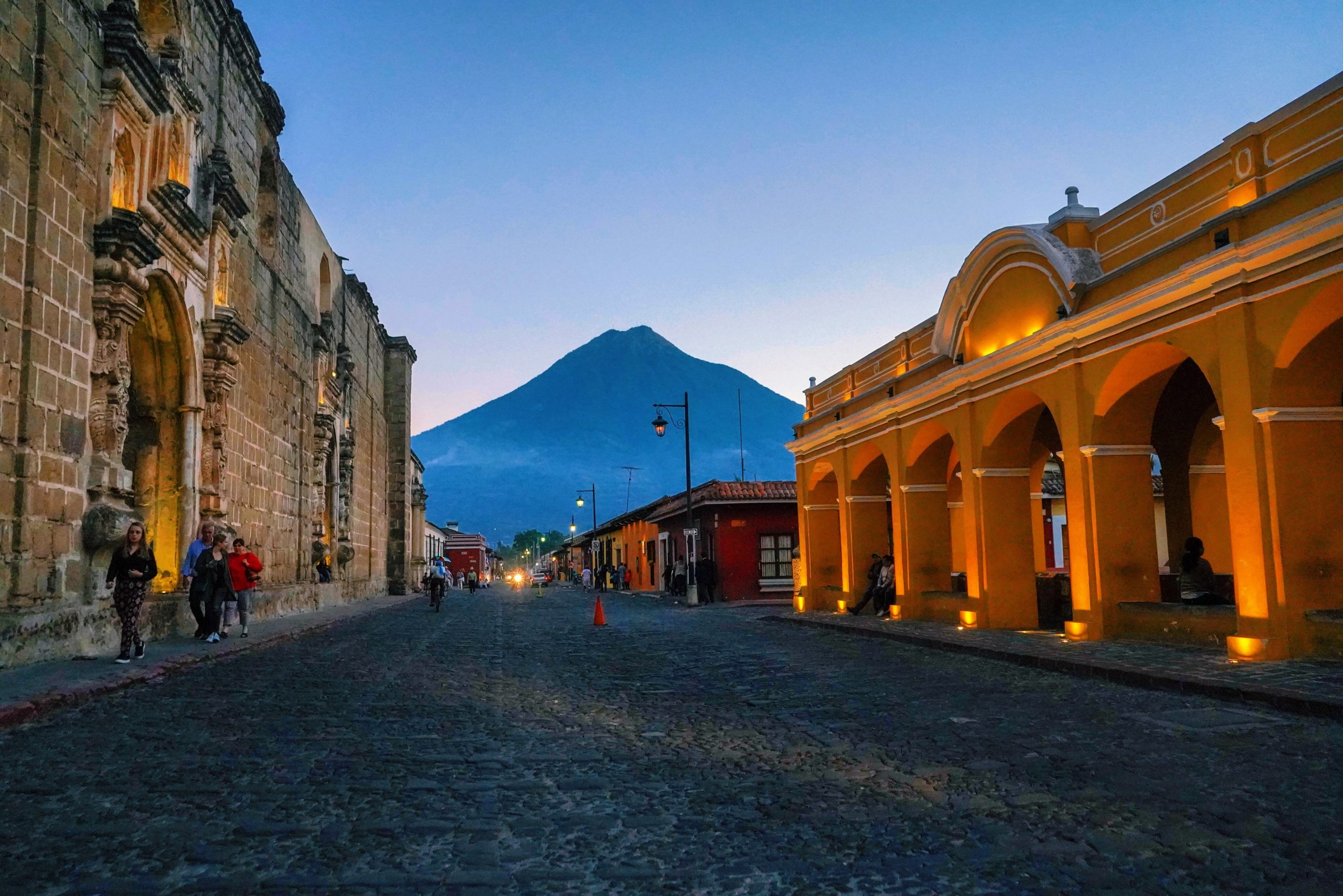 A cobblestone street in Antigua, a colonial city in Guatemala, glows at dusk beneath a volcano