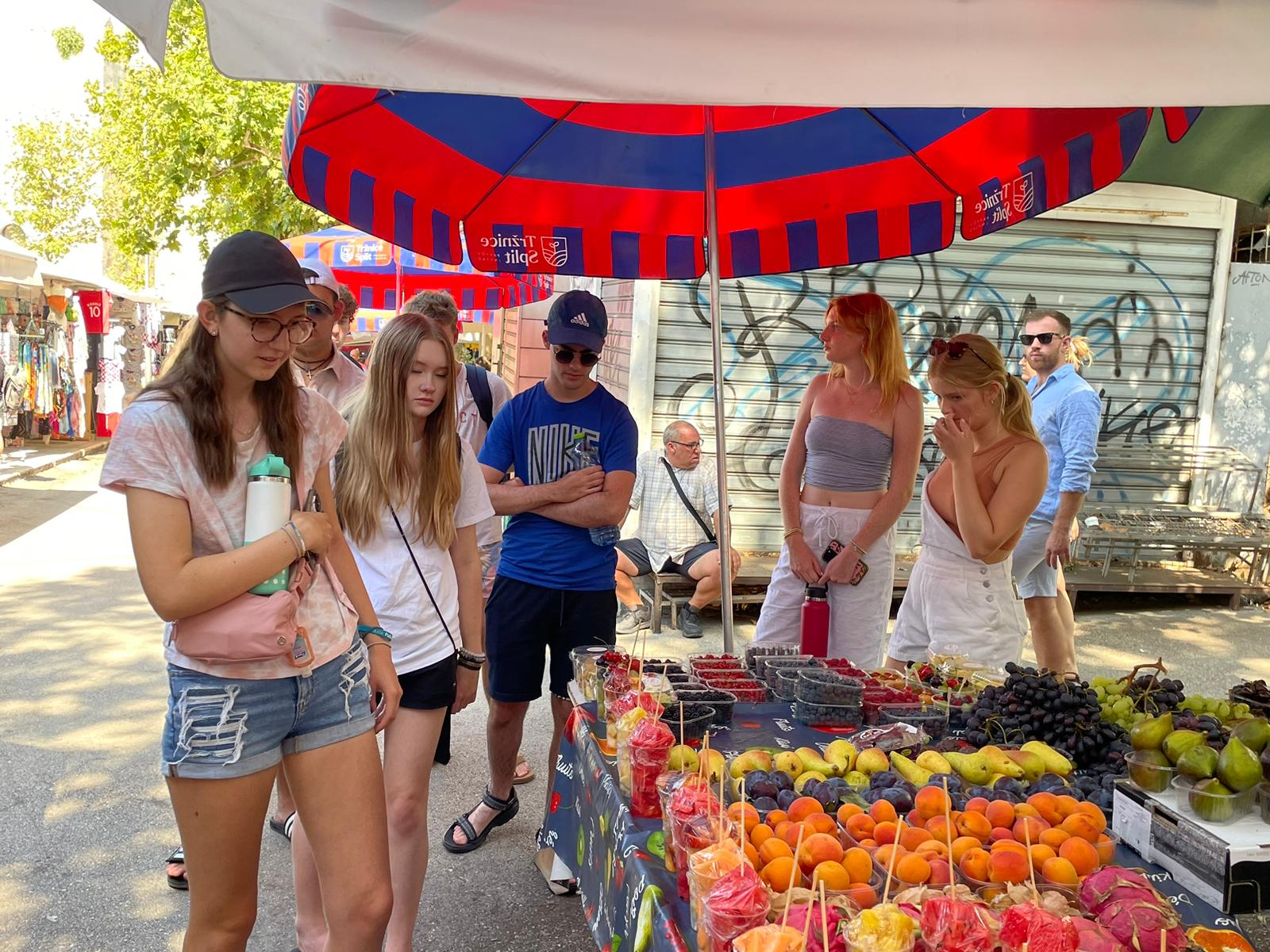 A Split market stall piled with apricots, plums, figs and grapes under red and blue umbrellas.