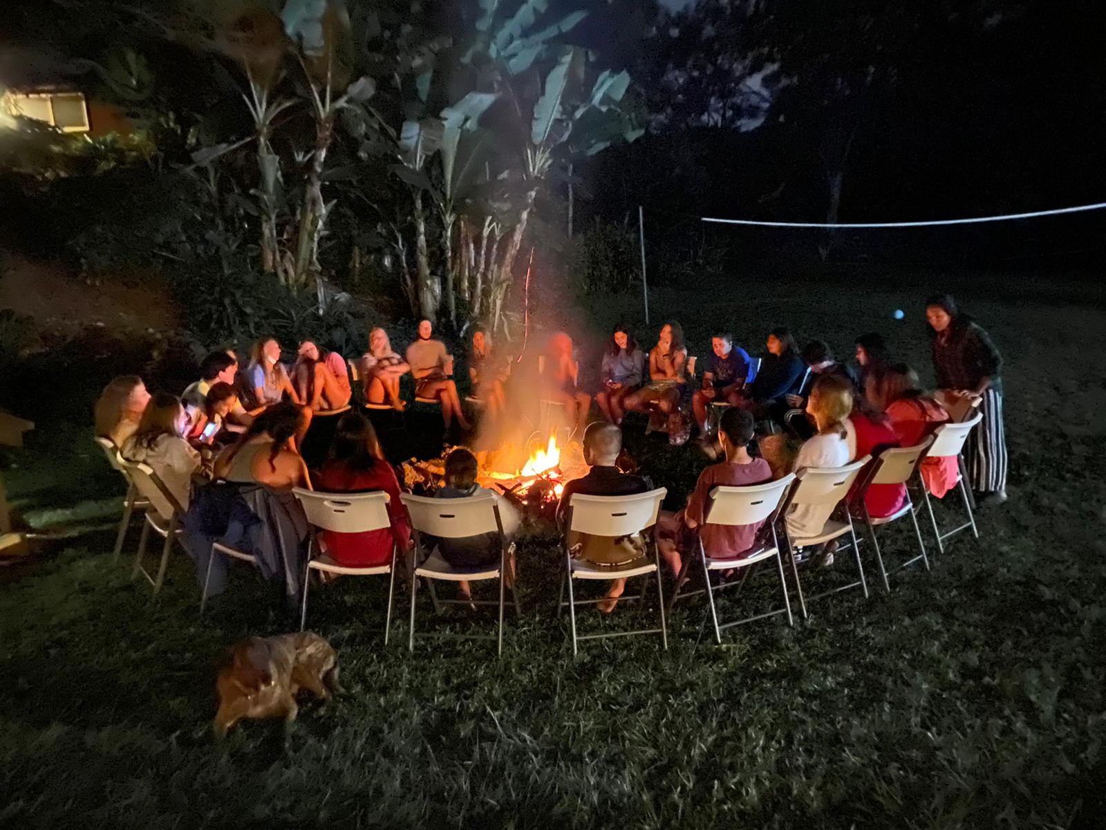 Students in the United States gather in chairs around a campfire at night