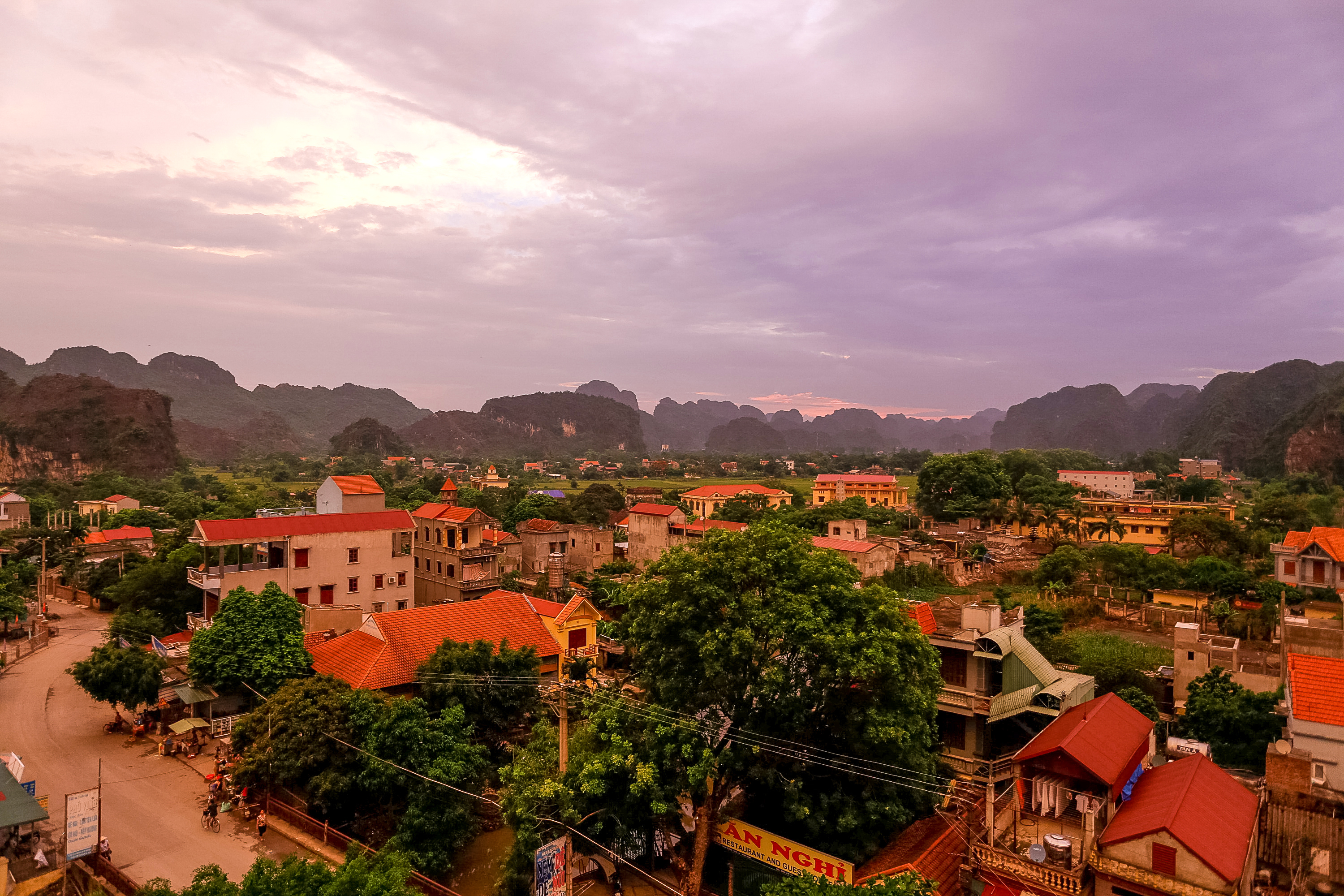 Rooftop view of a Vietnamese town with red-tiled roofs and limestone karst mountains at dusk