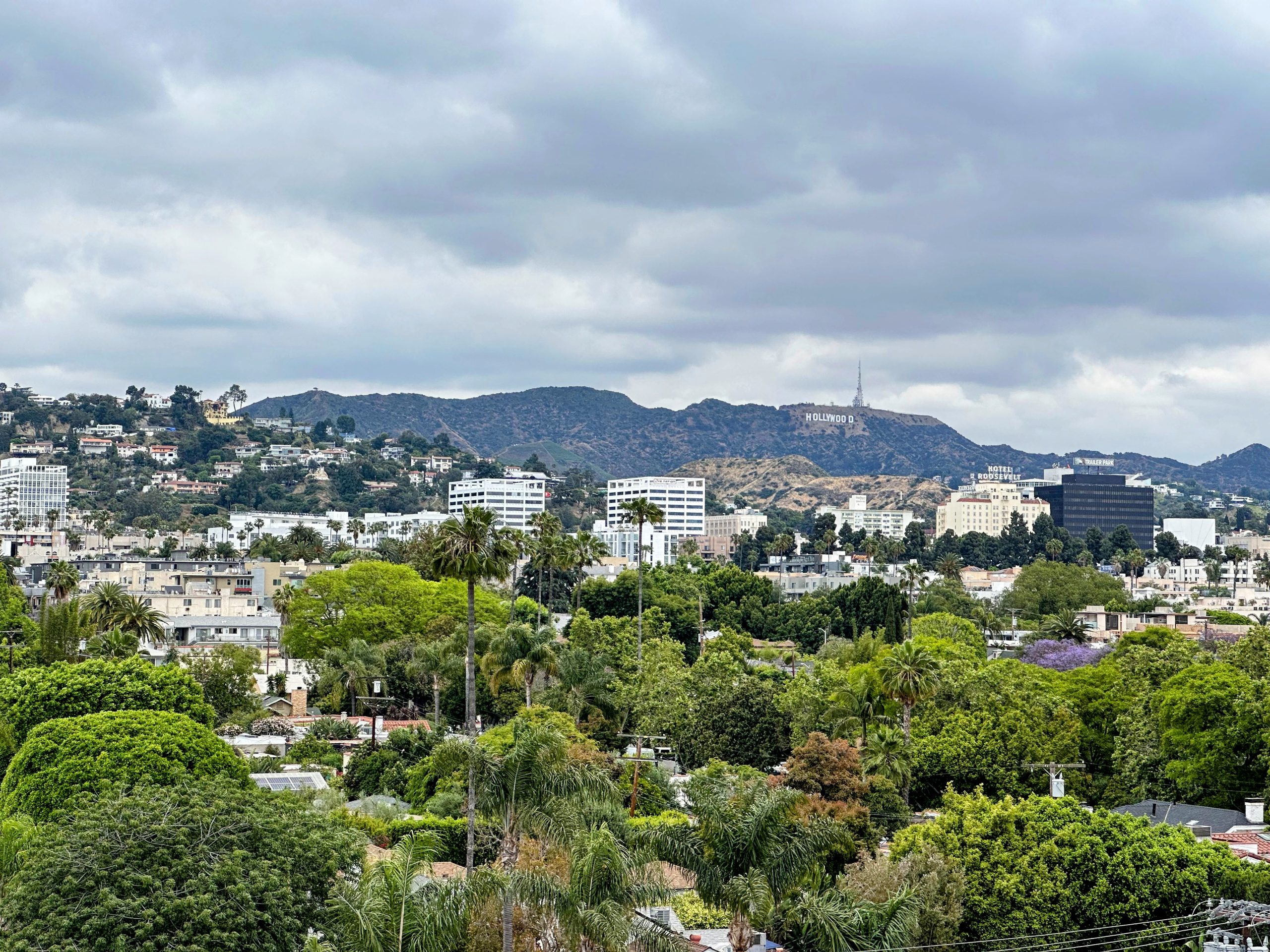 View of the Hollywood sign with lush green hills and city buildings in the foreground.