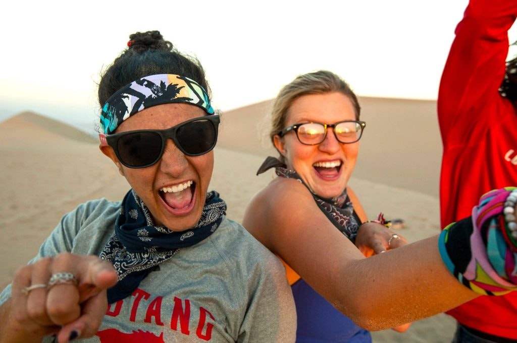 Two students laughing with sand dunes in the background.