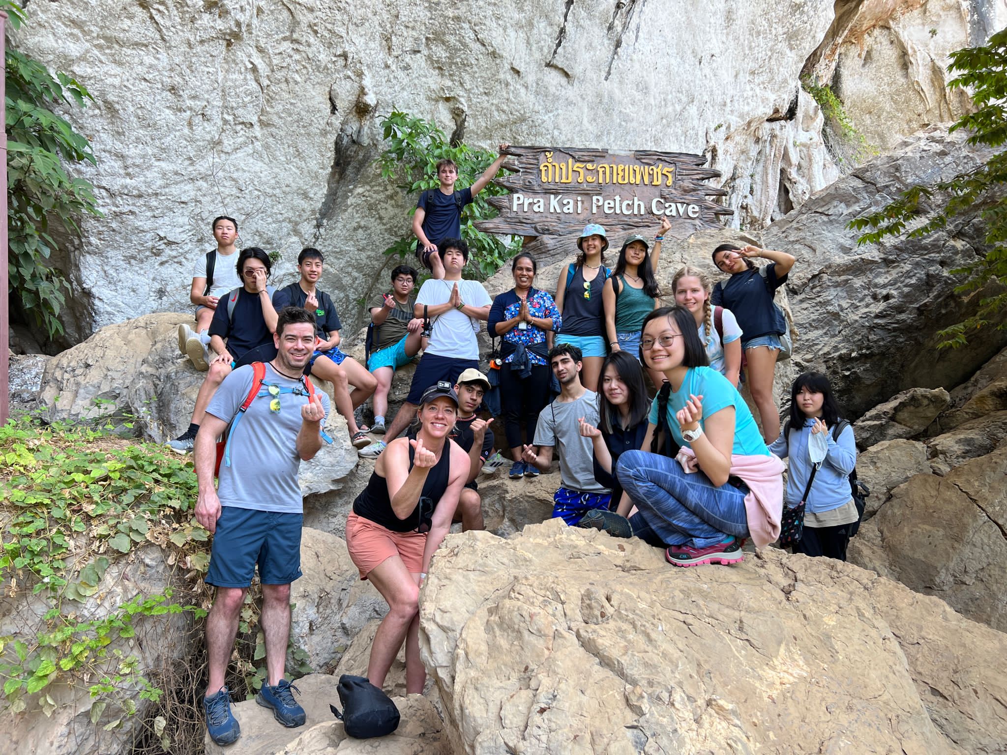 Students pose on rocks by the Pra Kai Pelch Cave sign