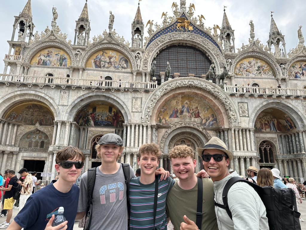Group of students smiling in front of St. Mark&rsquo;s Basilica during a Rustic Pathways European adventure teen tour.