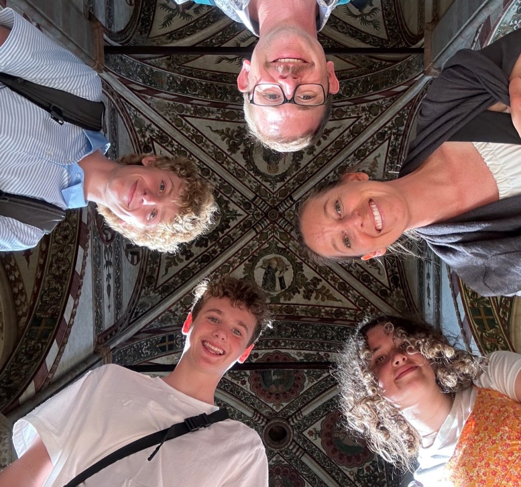 Five students smiling up at a beautifully painted ceiling with intricate patterns and religious artwork, participating in one of the best things you can do in Italy.