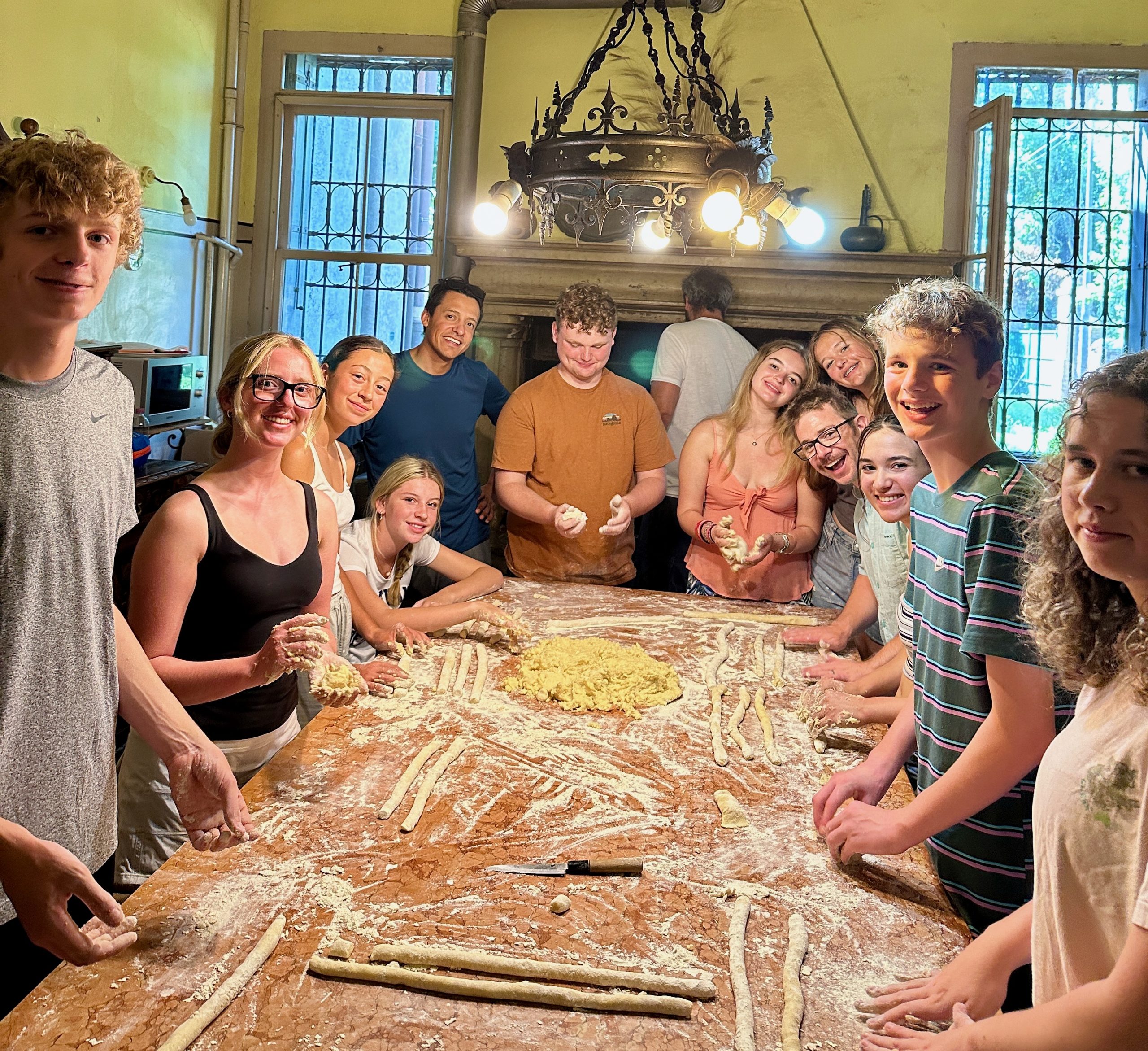 Teens gather around a floured table making handmade pasta
