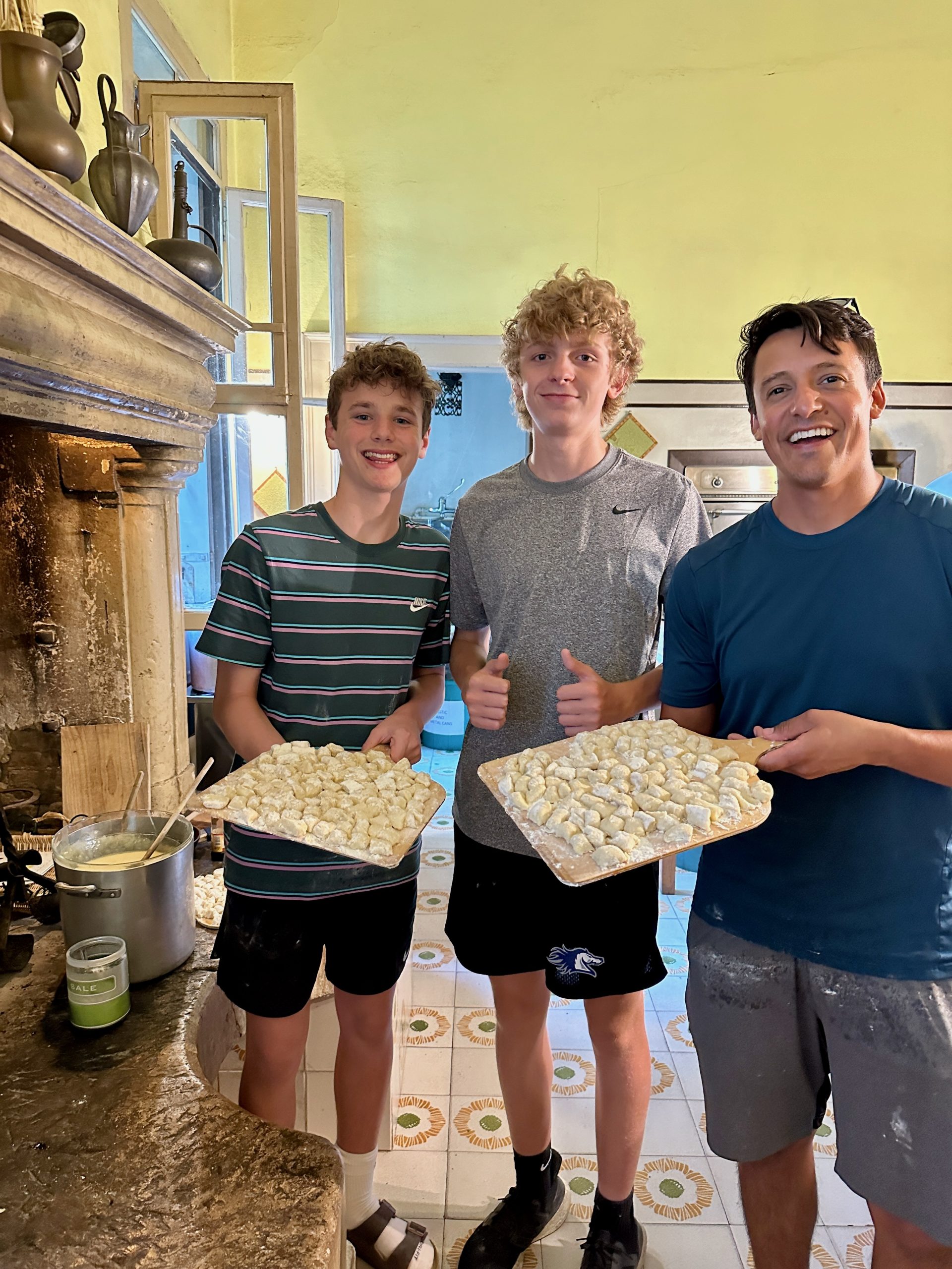 Students hold trays of freshly made gnocchi beside a stone fireplace