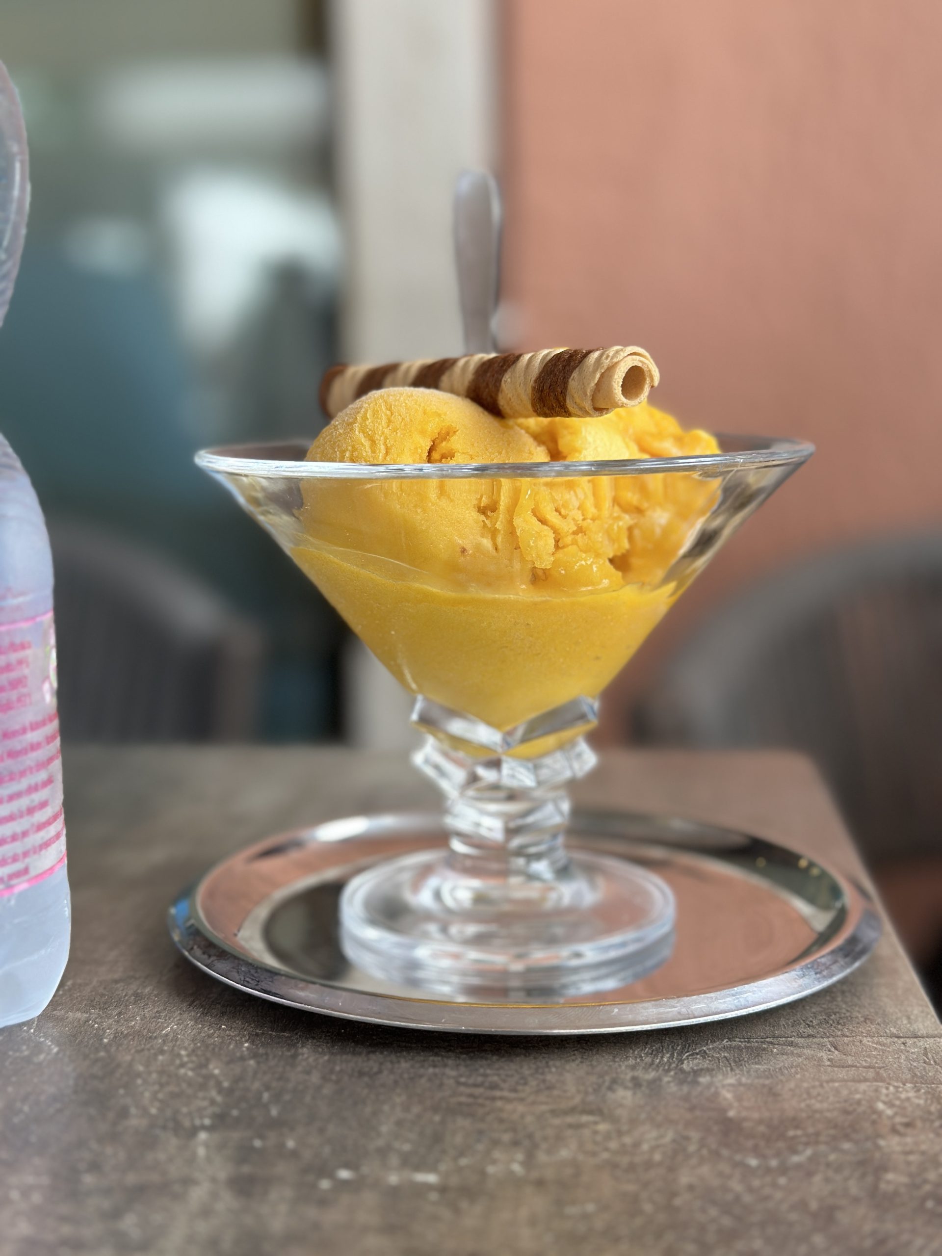 A scoop of mango gelato with a rolled wafer cookie in a glass dish
