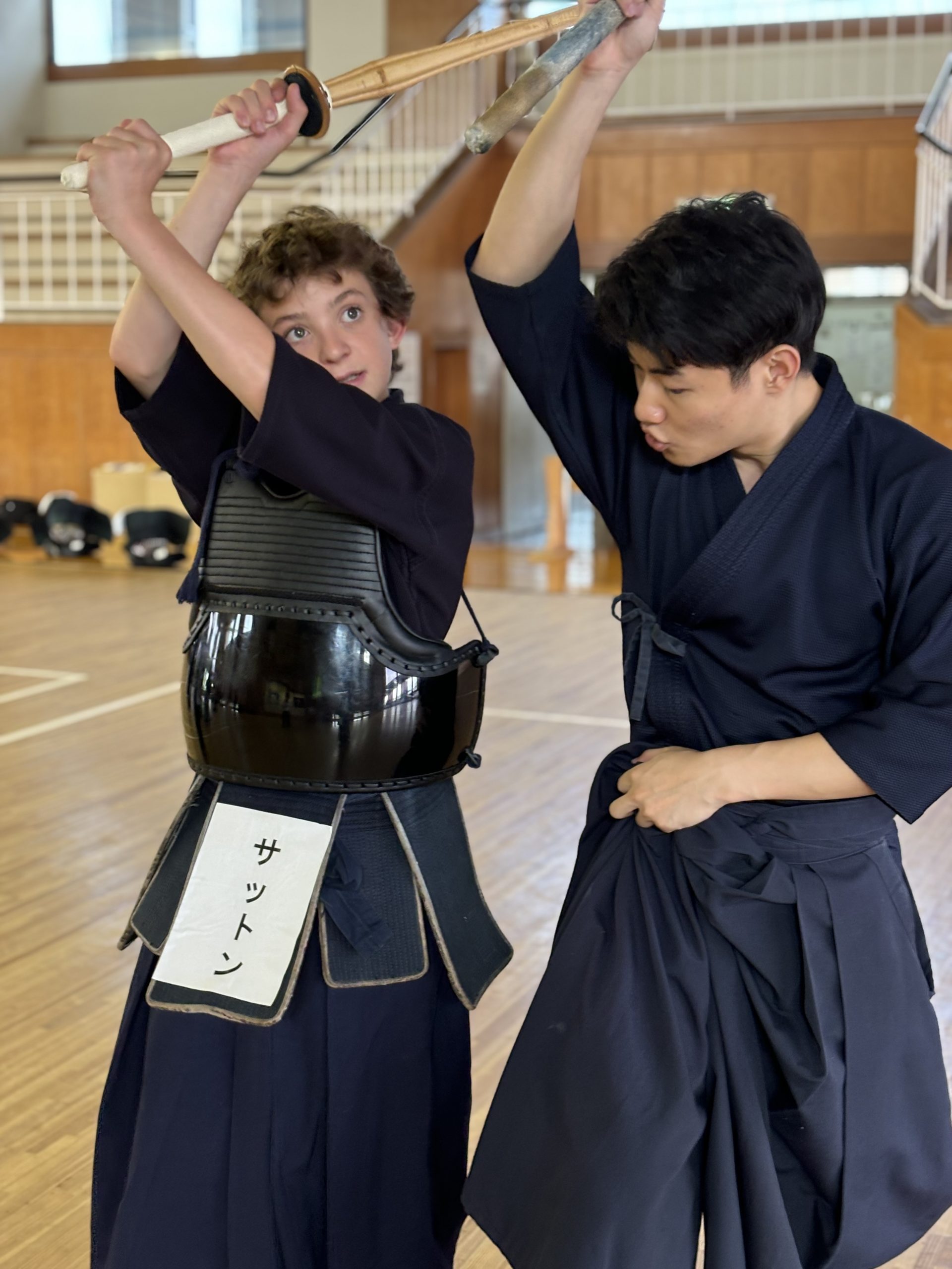 Teen travelers raise bamboo swords overhead in kendo armor during a lesson