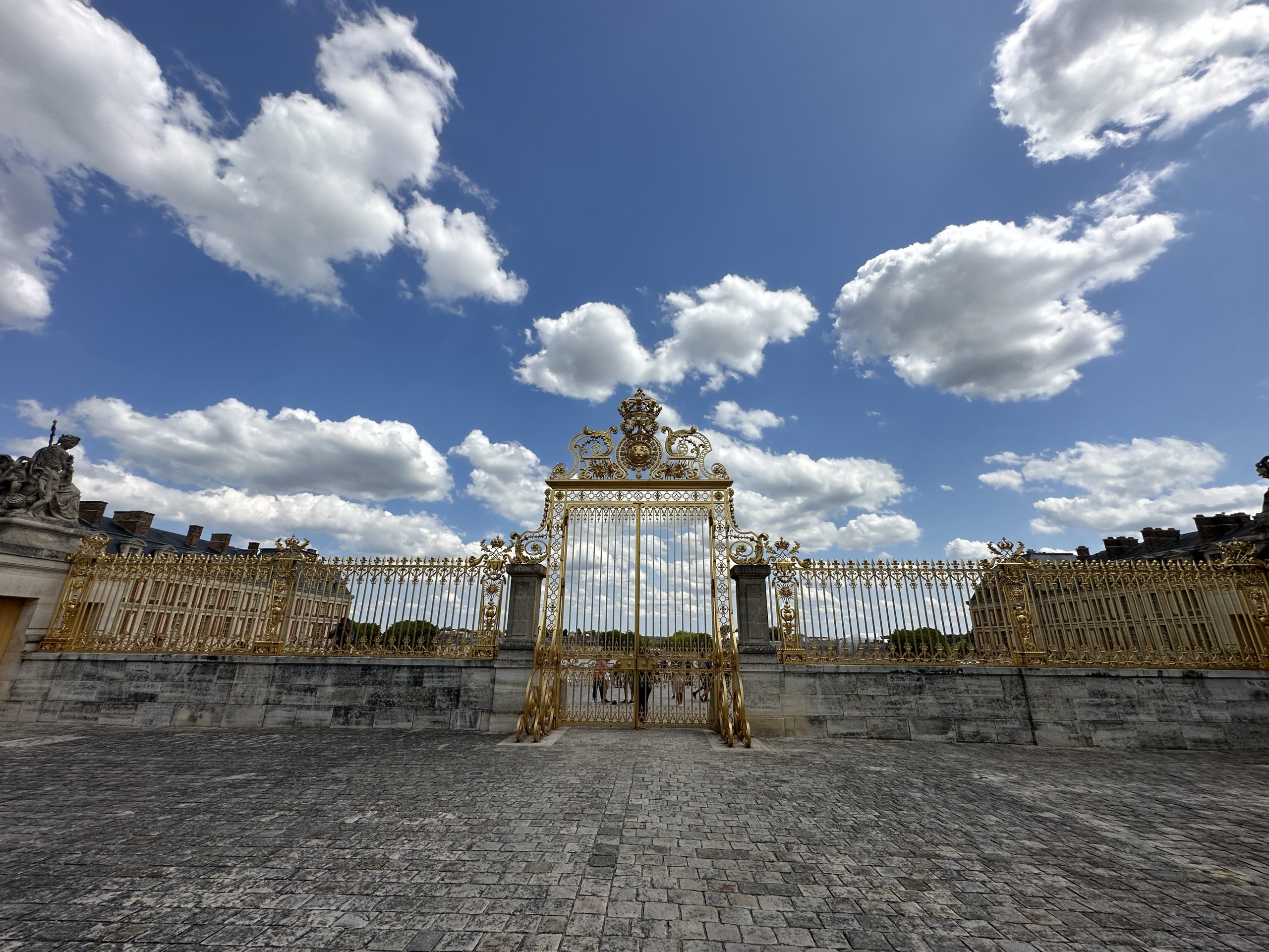 Ornate golden gate at the Palace of Versailles under a partly cloudy sky