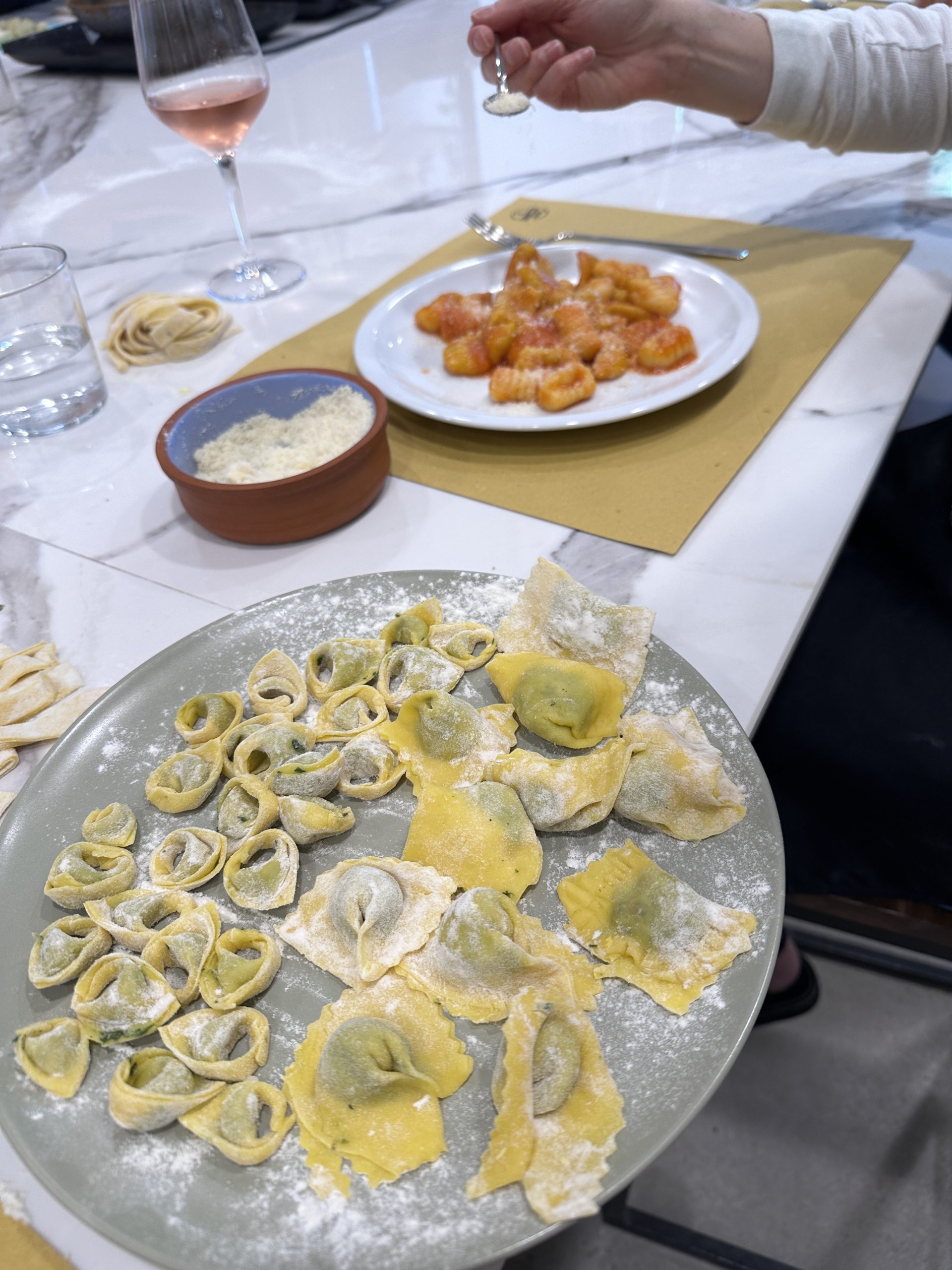 Handmade tortellini and ravioli dusted with flour on a plate, with gnocchi and grated cheese in the background