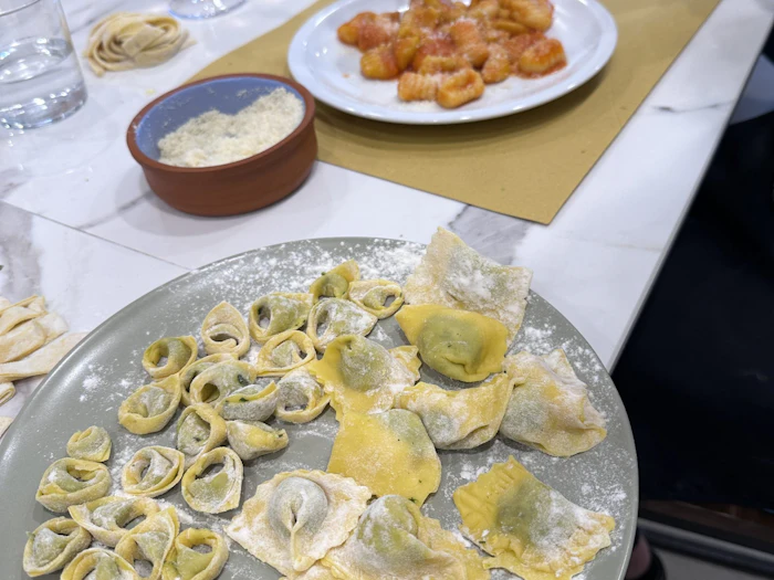 Hand-shaped tortellini and ravioli, still dusted with flour, laid out on a plate beside gnocchi and grated cheese.