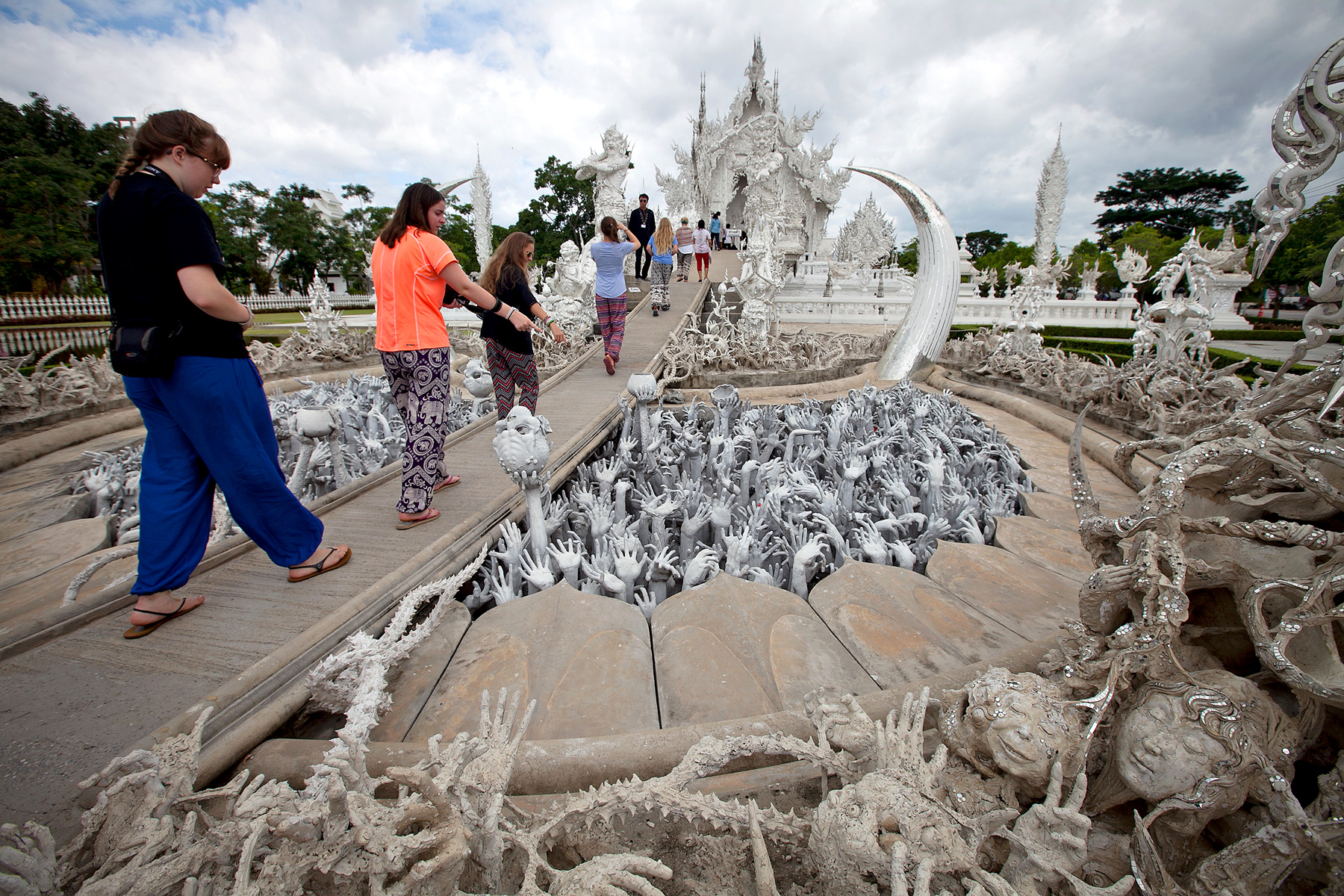 Students walk the bridge over sculpted hands at Wat Rong Khun's White Temple