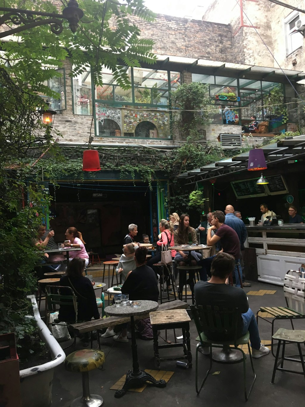 People relax at a bar in Budapest. The rustic interior features green trees.