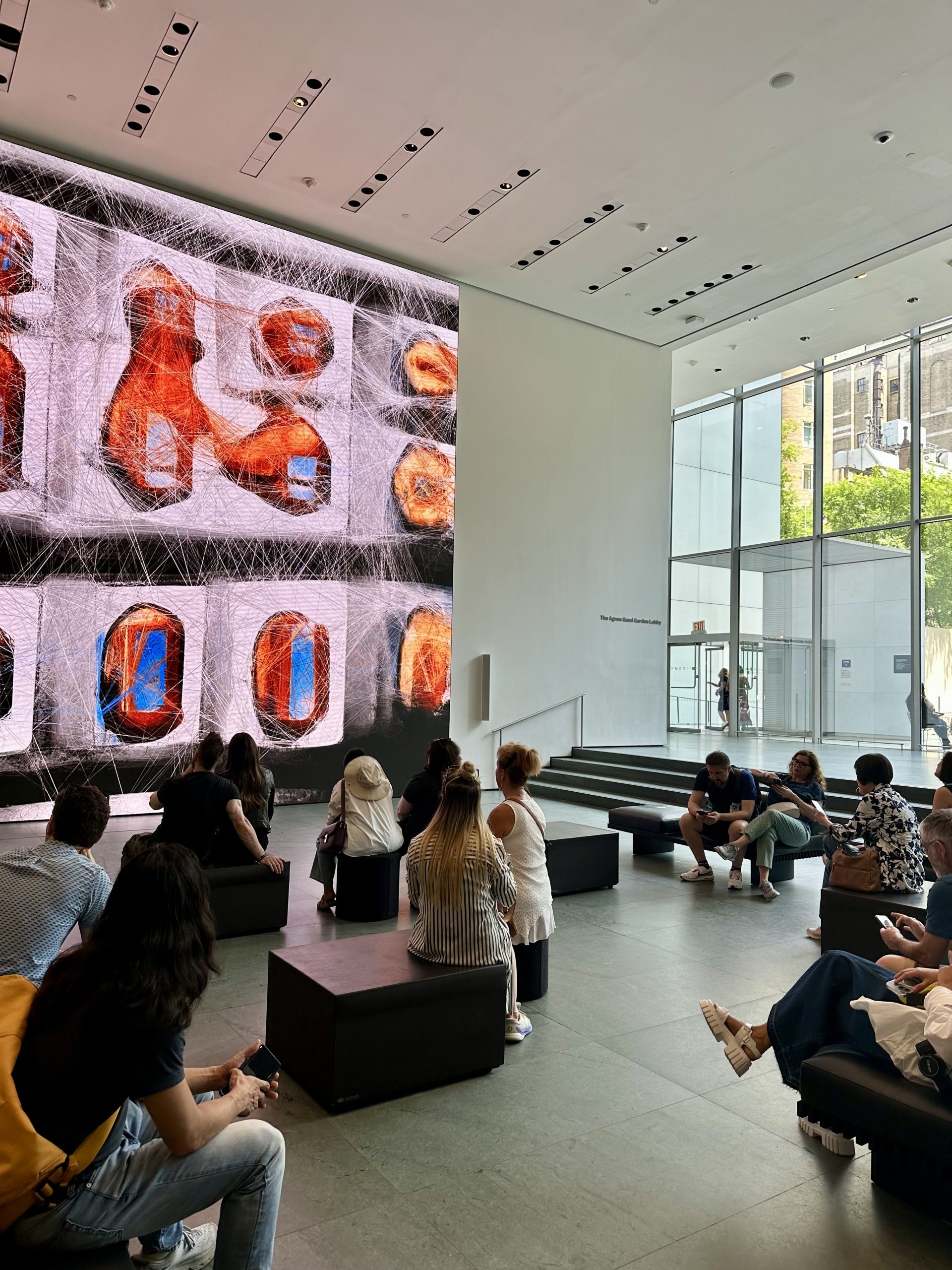 Students sit on benches viewing a large digital art installation in a museum gallery