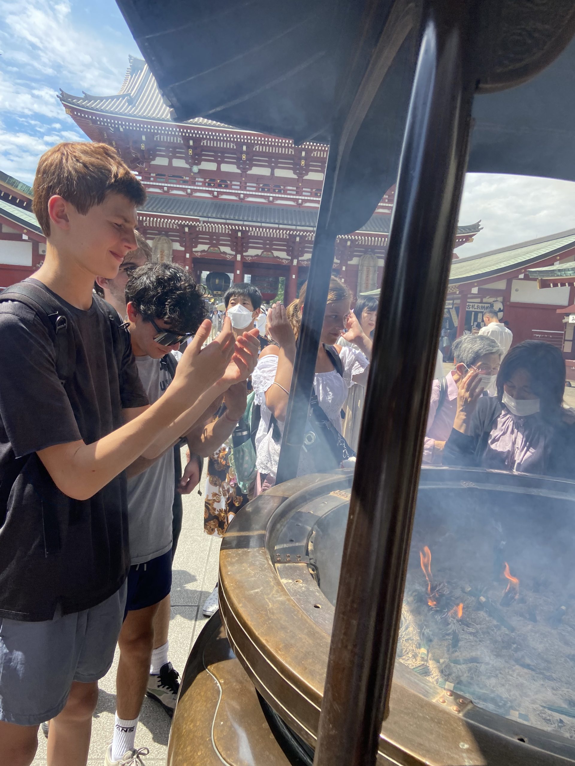 A student wafts incense smoke over an urn at a temple, with a pagoda rising behind