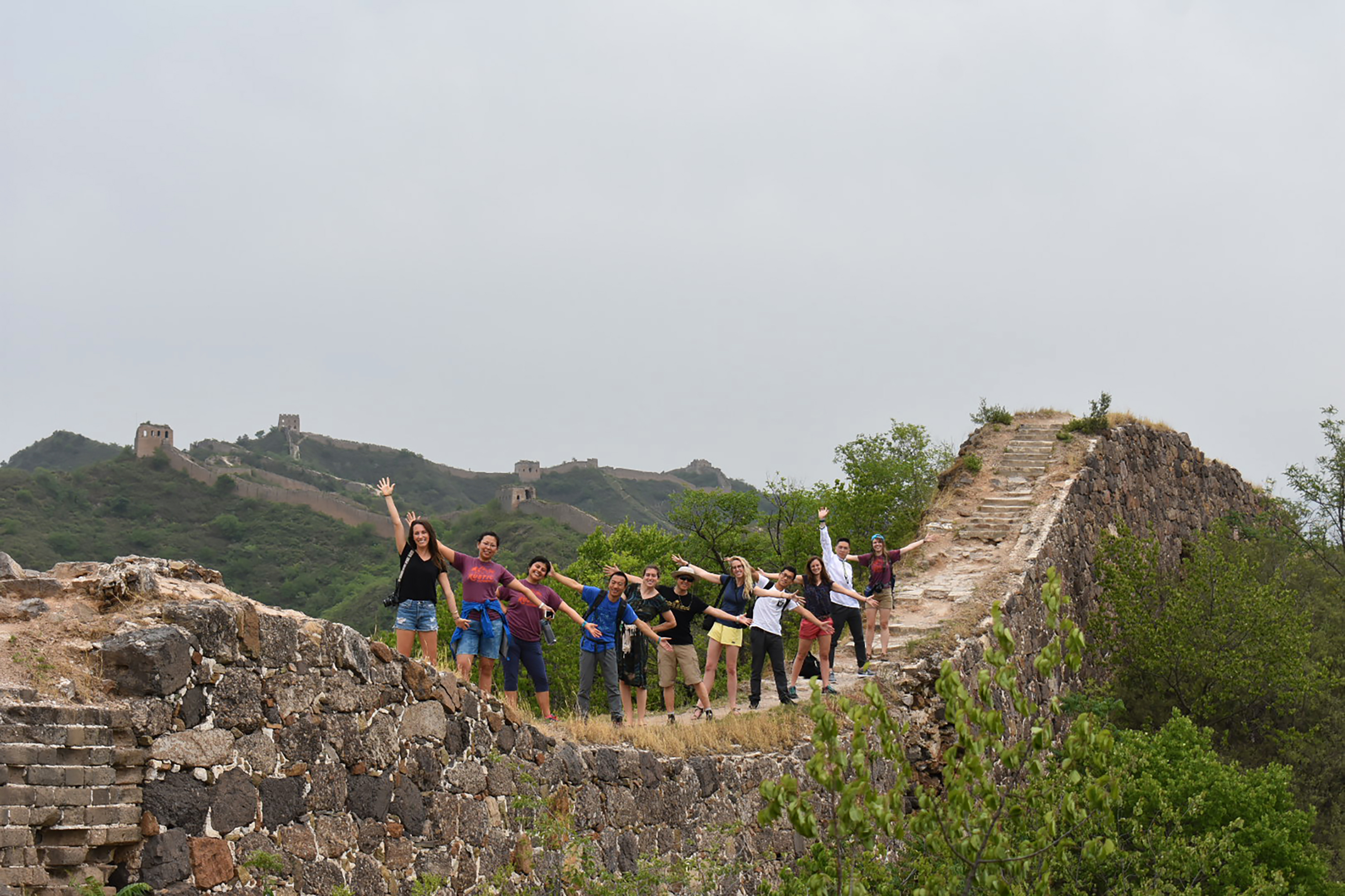 Teen travelers pose with raised arms atop a remote, unrestored section of the Great Wall