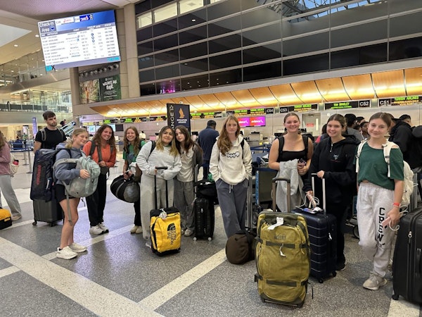 Group of teens standing near the airport check-in counters with their suitcases and luggage.