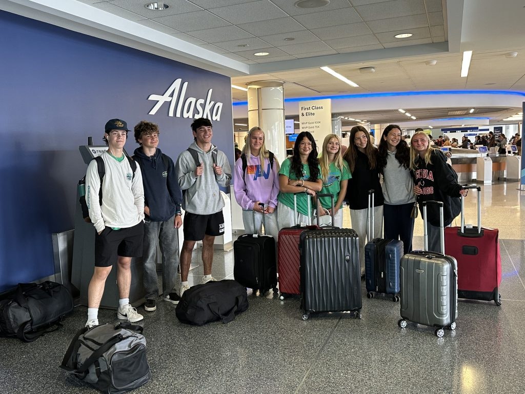 Group of teens standing near the airport check-in counters with their suitcases and luggage.