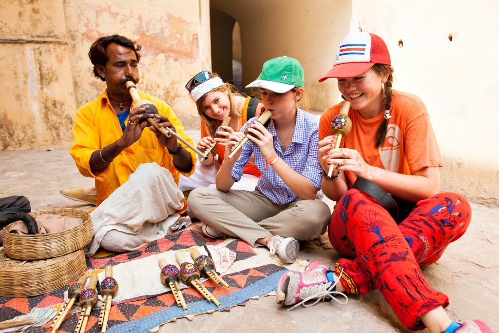 A group of teen travelers playing traditional flutes with a merchant during a cultural immersion teen tour in India.