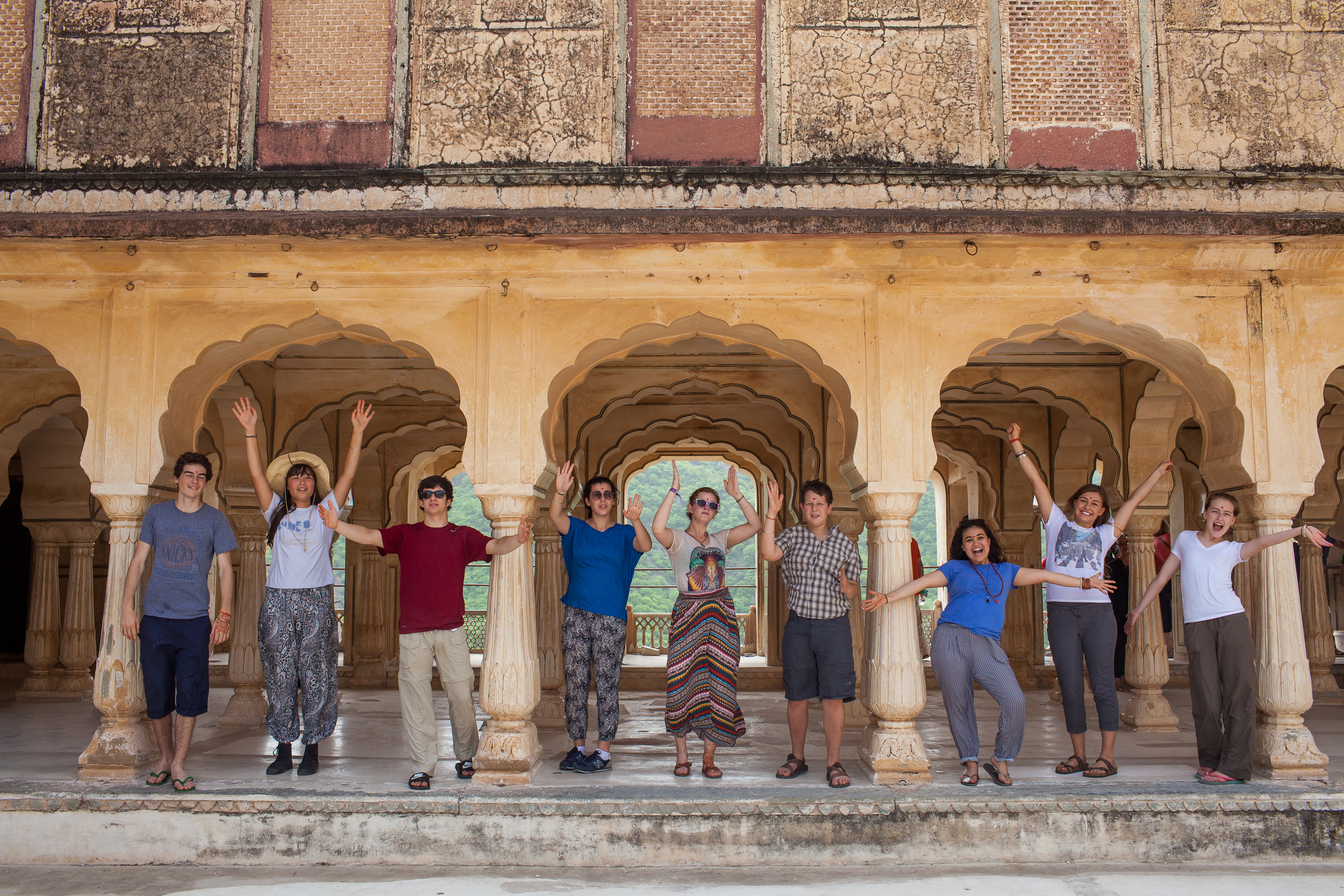 Students raise their arms while posing along a sandstone arched colonnade